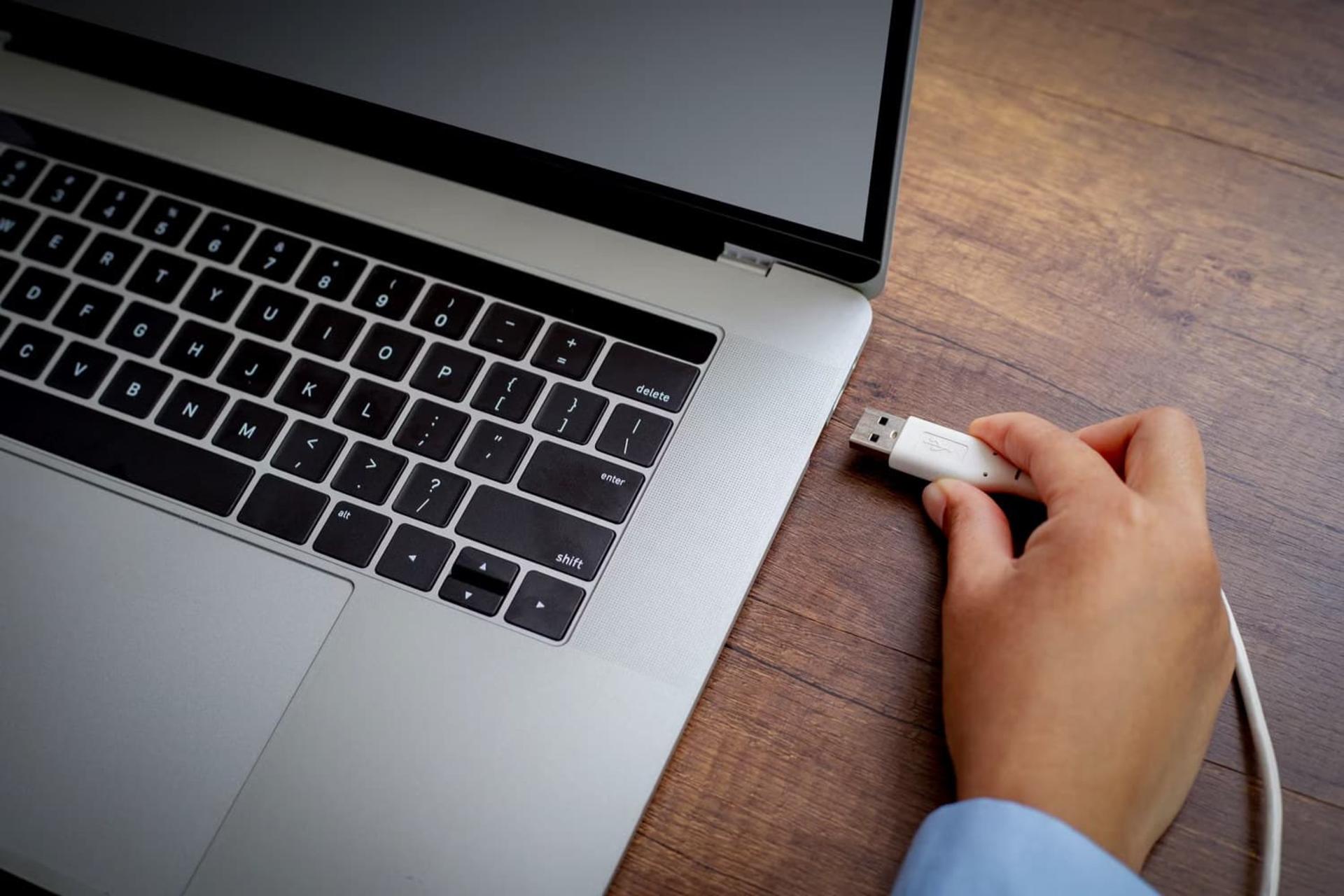 دستی در حال نگه داشتن کابل USB نزدیک پورت لپ‌تاپ
