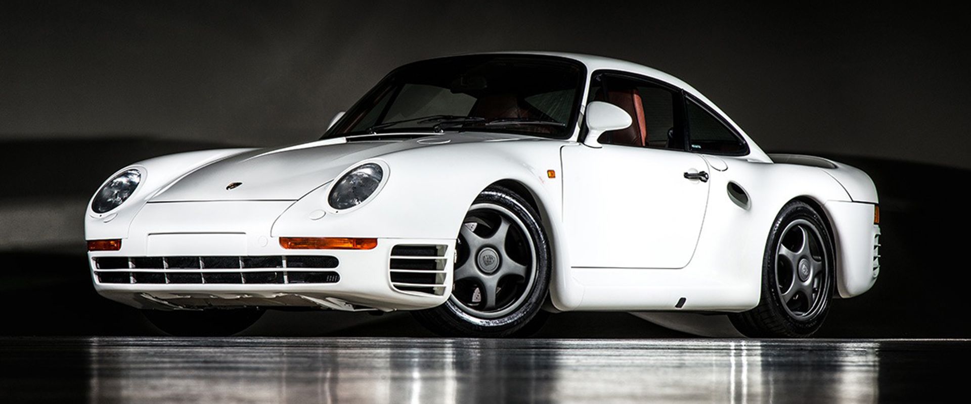 نمای کناری خودروی Porsche 959 Sport به رنگ سفید که انعکاس آن روی زمین دیده می شود