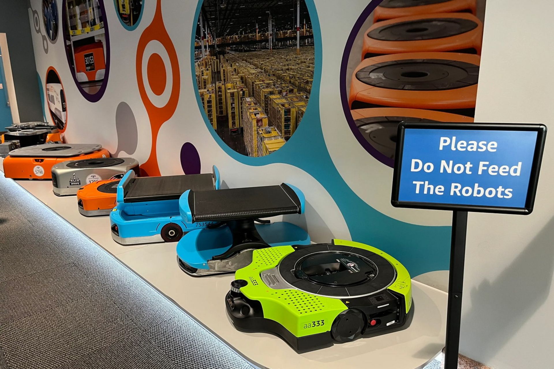 ردیف ربات‌های جدید و قدیمی آمازون با تابلوی «Please Do Not Feed The Robots»