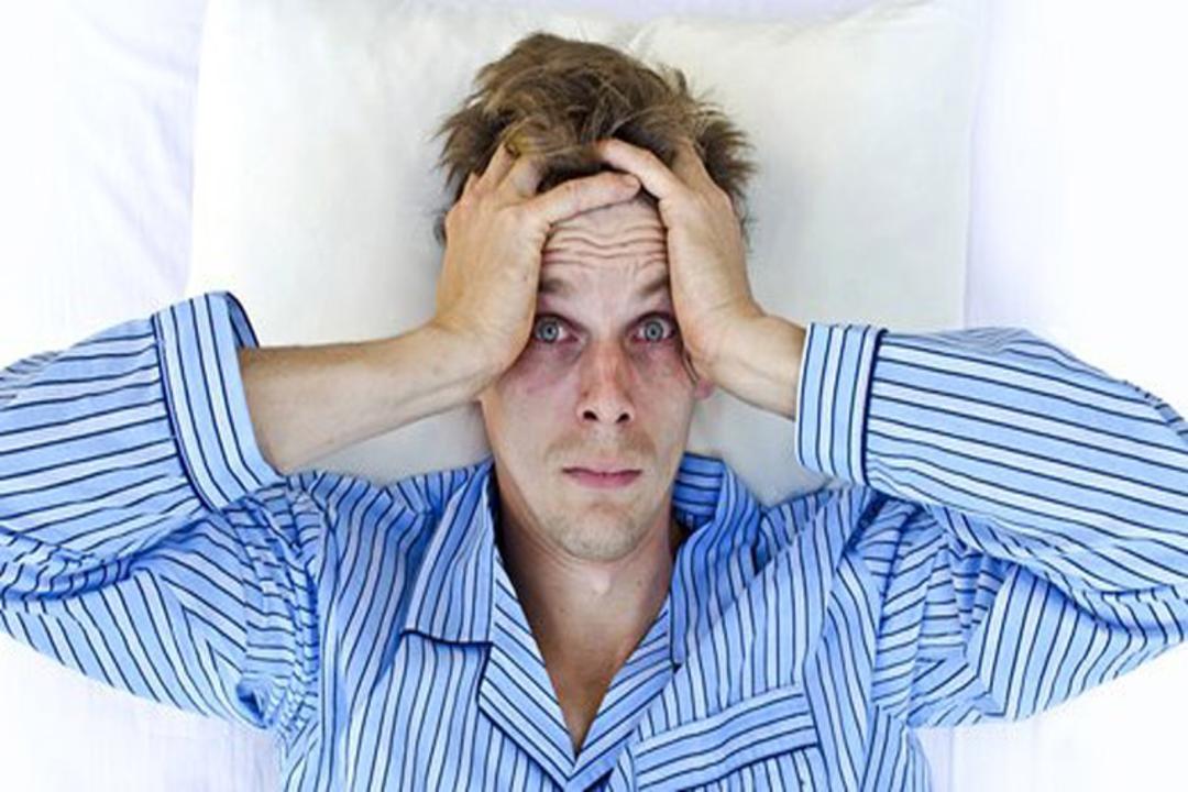 مرد با لباس آبی راه راه کلافه دست روی سر کم خواب
