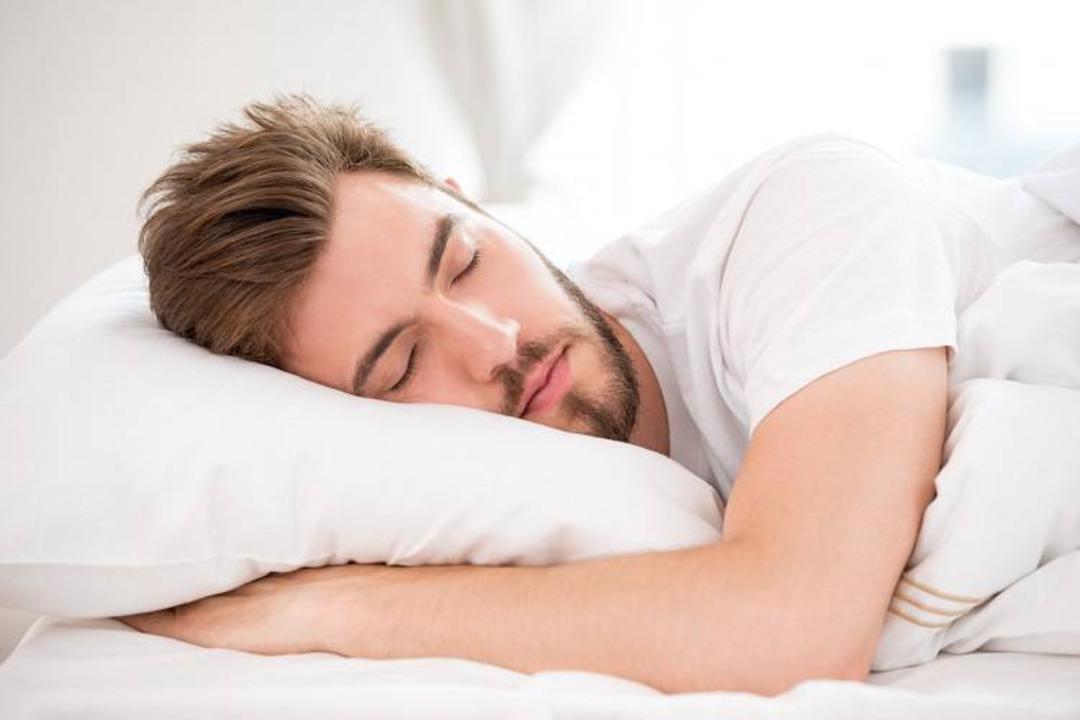 مرد ریشو با لباس سفید درحال خواب روی بالش و پتو سفید
