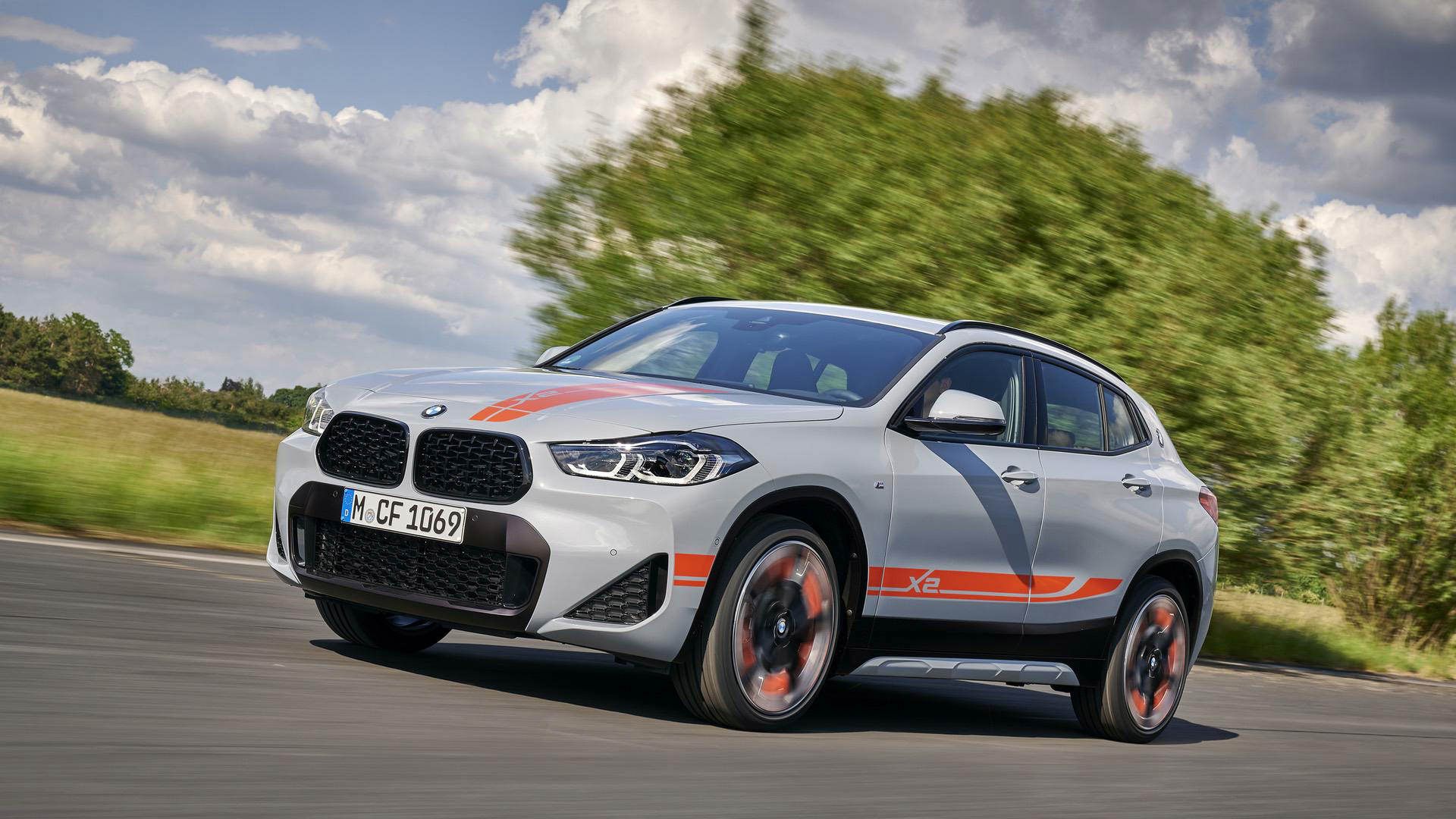 نمای سه چهارم جلو کراس اور بی ام و ایکس 2 / BMW X2 M Mesh Edition نقره ای رنگ در کنار درخت و آسمان ابری و جاده