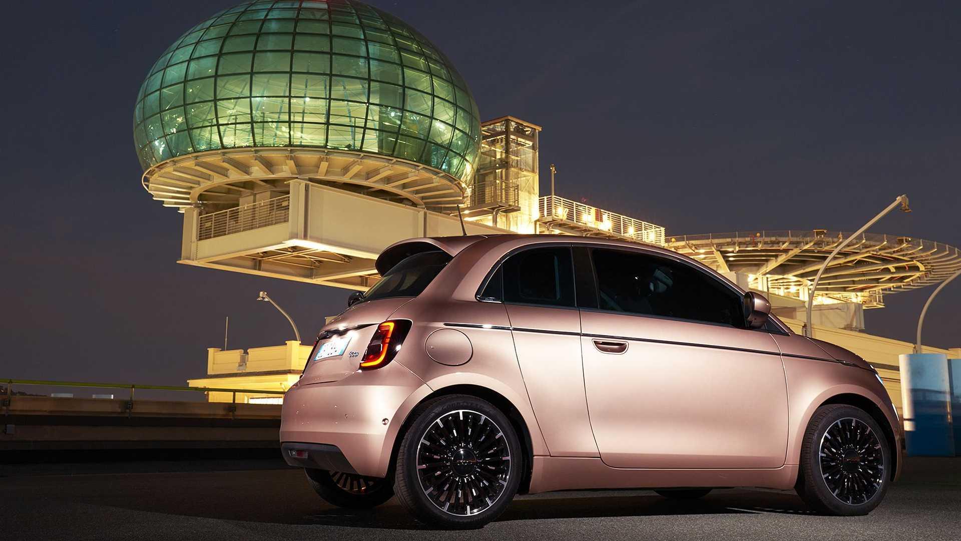 نمای جانبی خودروی الکتریکی فیات 500 / Fiat 500 Electric در کنار سازه معماری در شب