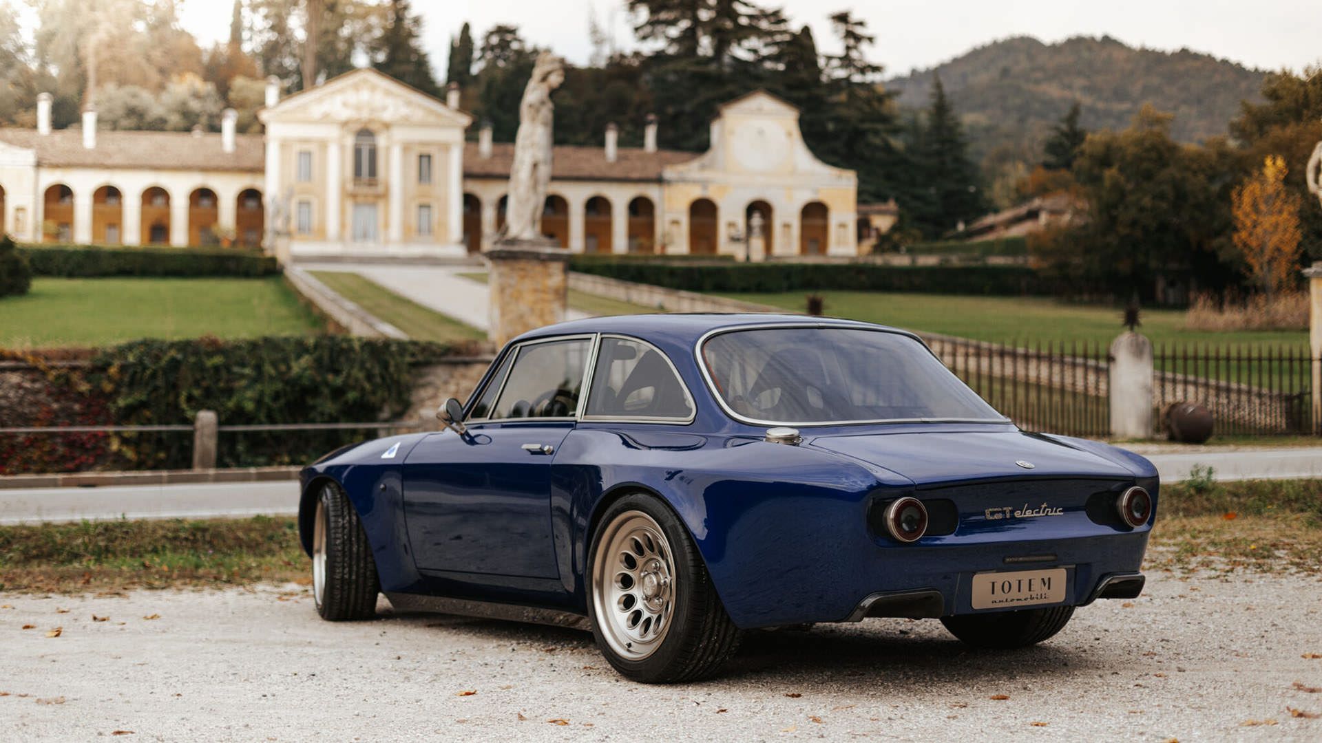 نمای سه چهارم عقب خودروی الکتریکی آلفا رومئو جولیا / Alfa Romeo Giulia GTA آبی رنگ در کنار ساختمان