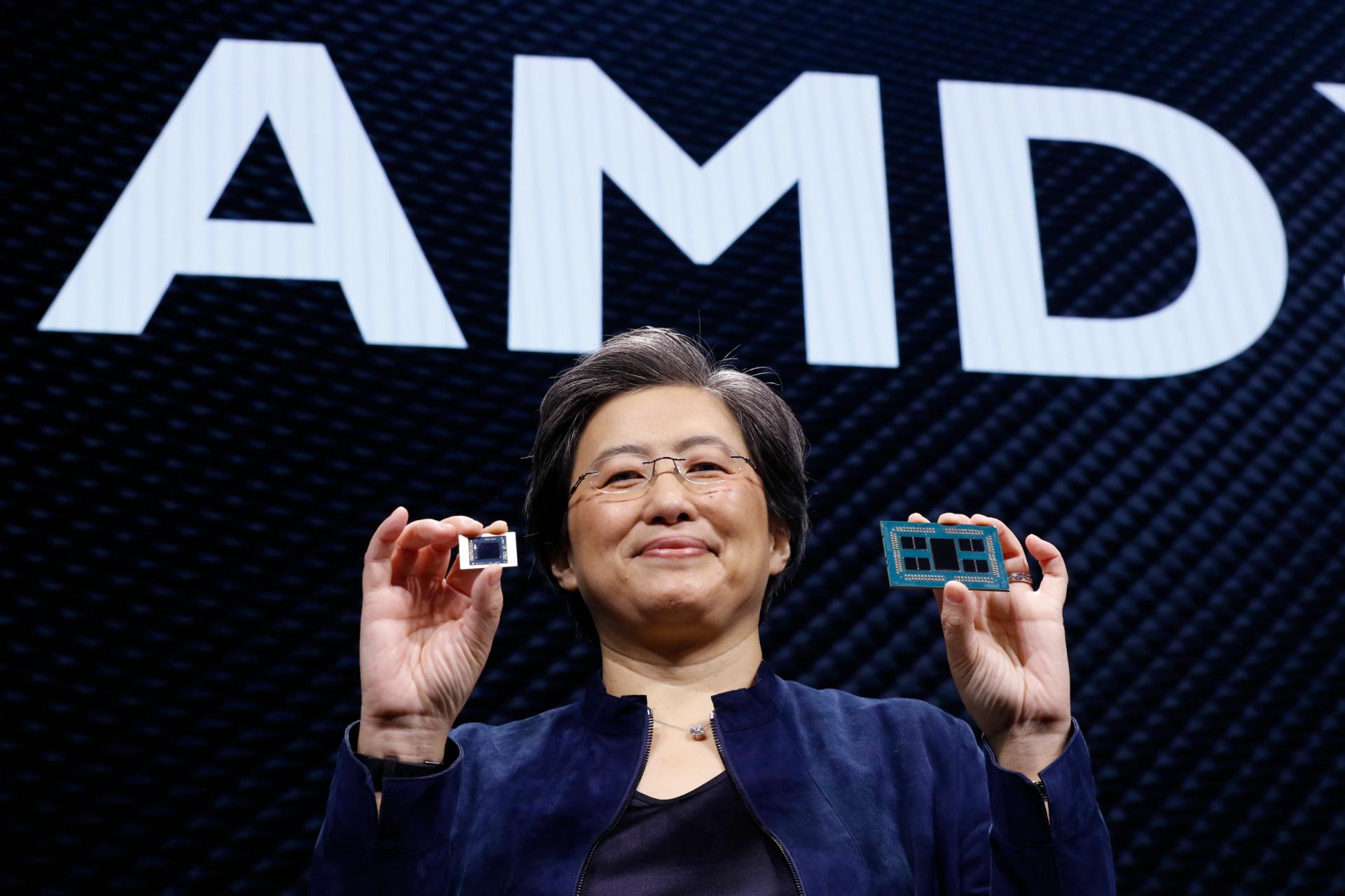 دکتر لیزا سو مدیرعامل ای ام دی / AMD CEO Lisa Su درحال لبخند در جلوی لوگو شرکت با دو تراشه