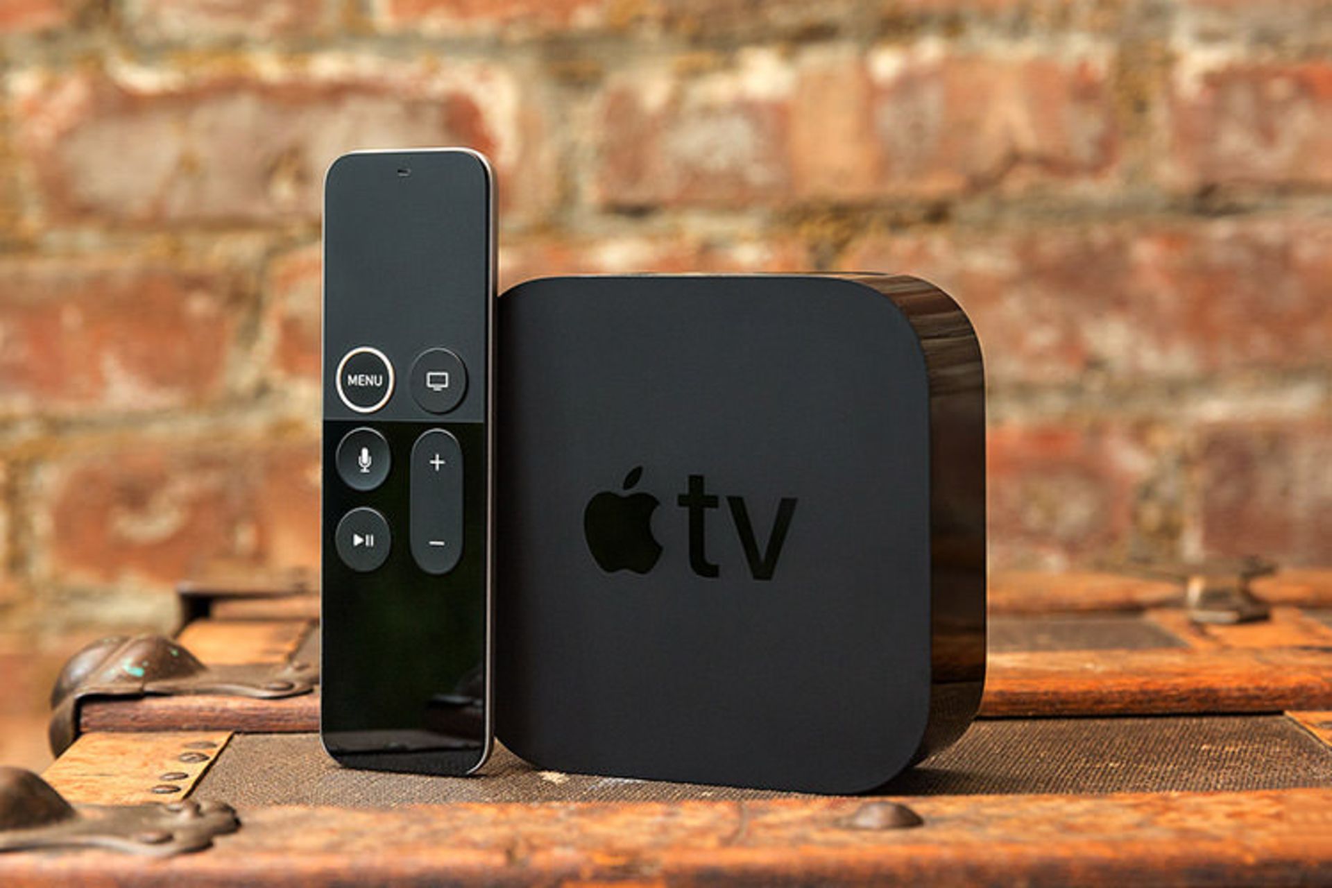 اپل تی وی / Apple TV با ریموت کنترل روی میز جلوی دیوار آجری