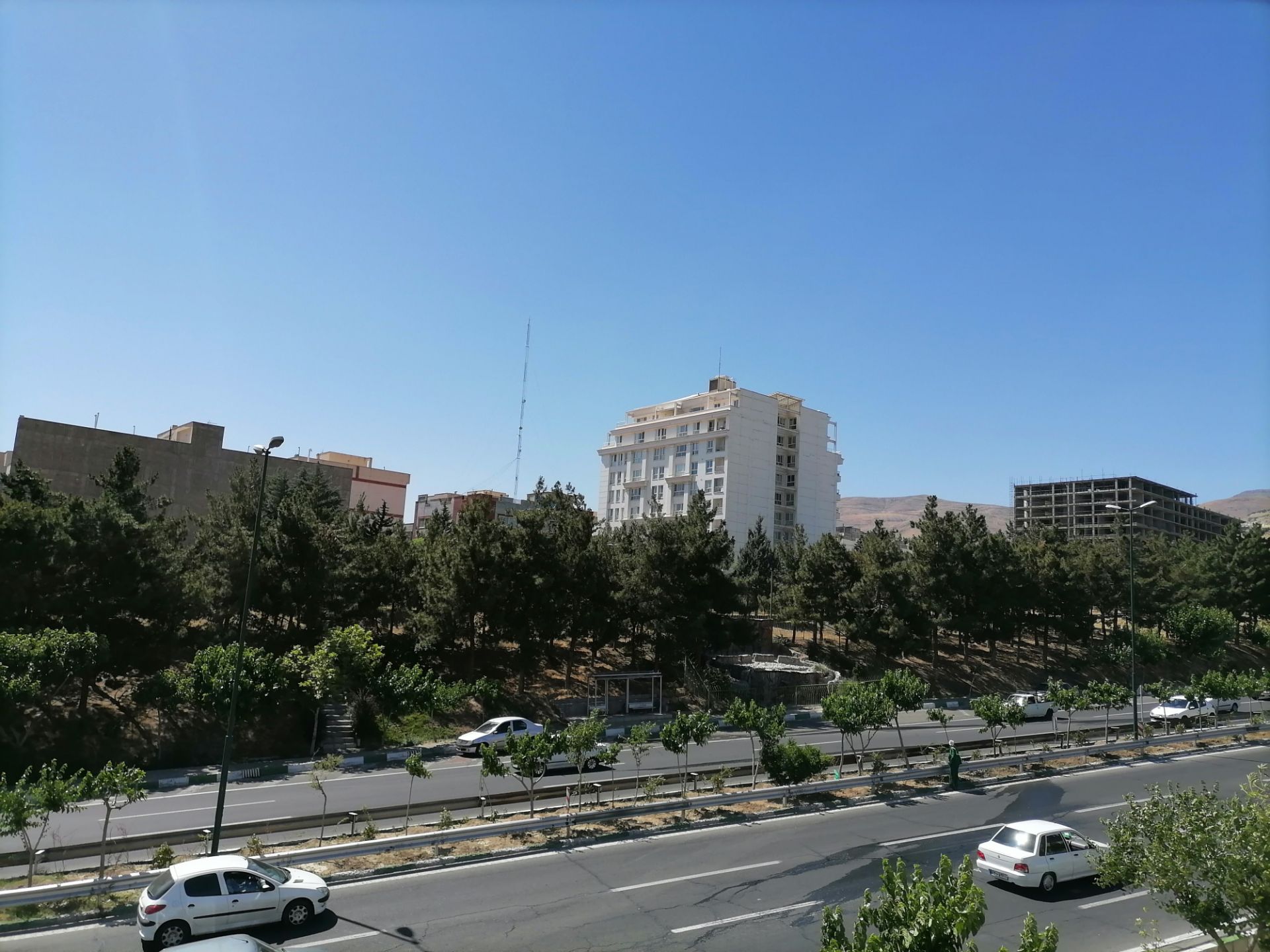 عکس واید از ساختمان‌ها و درختان کنار بزرگراه به همراه خودروهای در حال حرکت