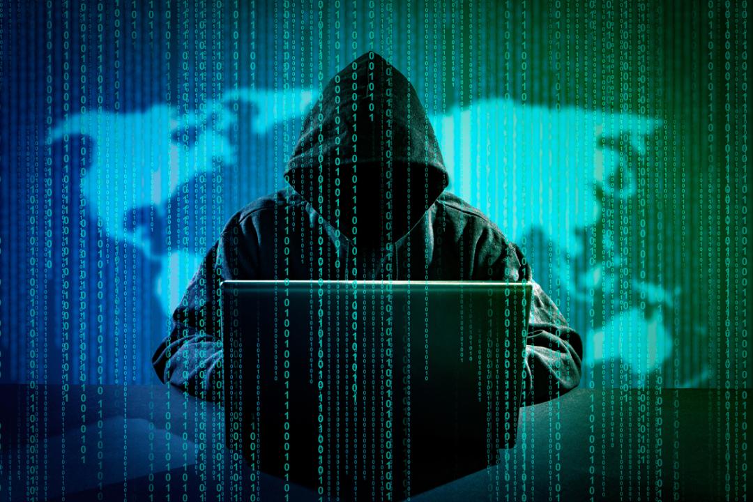 هکر با هودی مشکی پشت لپ تاپ در حال هک / Hacker