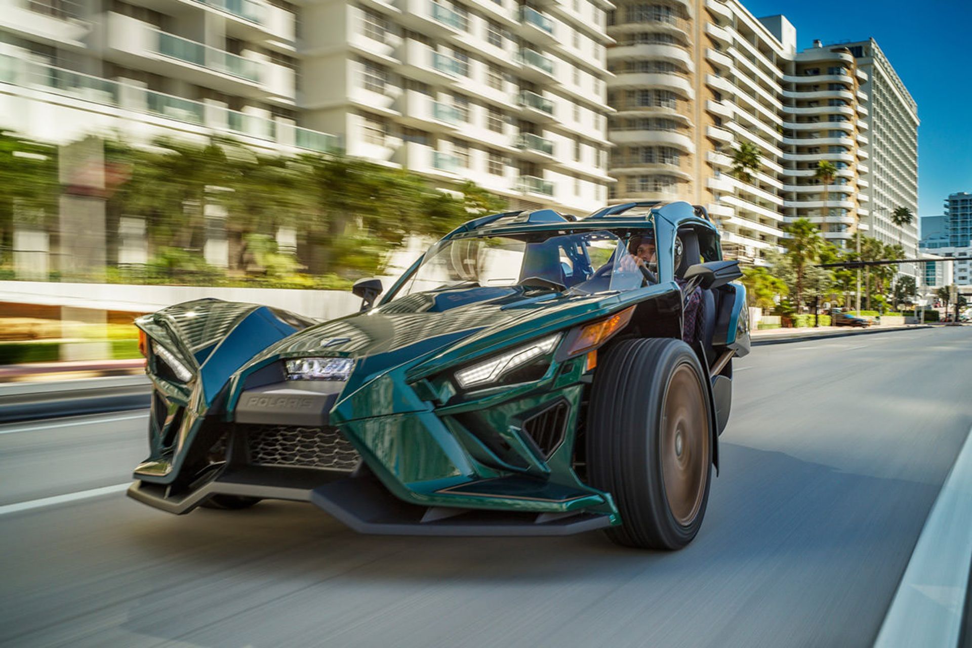 نمای جلو خودرو سه چرخ پولاریس اسلینگ شات گرند تورینگ / Polaris Slingshot Grand Touring LE با رنگ سبز در خیابان نزدیک ساختمان 