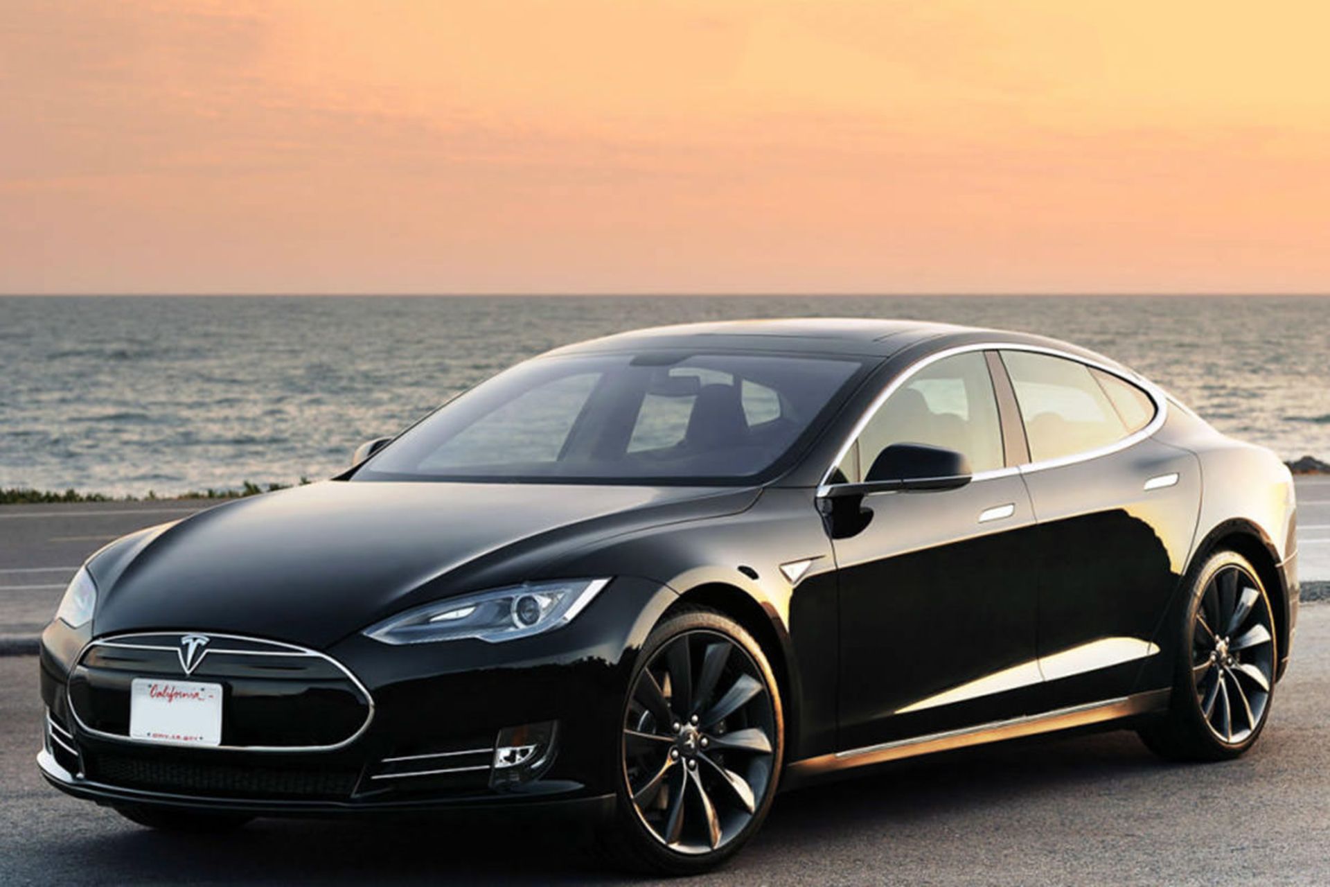 خودروی الکتریکی تسلا مدل اس / tesla model s electric car با رنگ مشکی در کنار ساحل دریا هنگام غروب آفتاب
