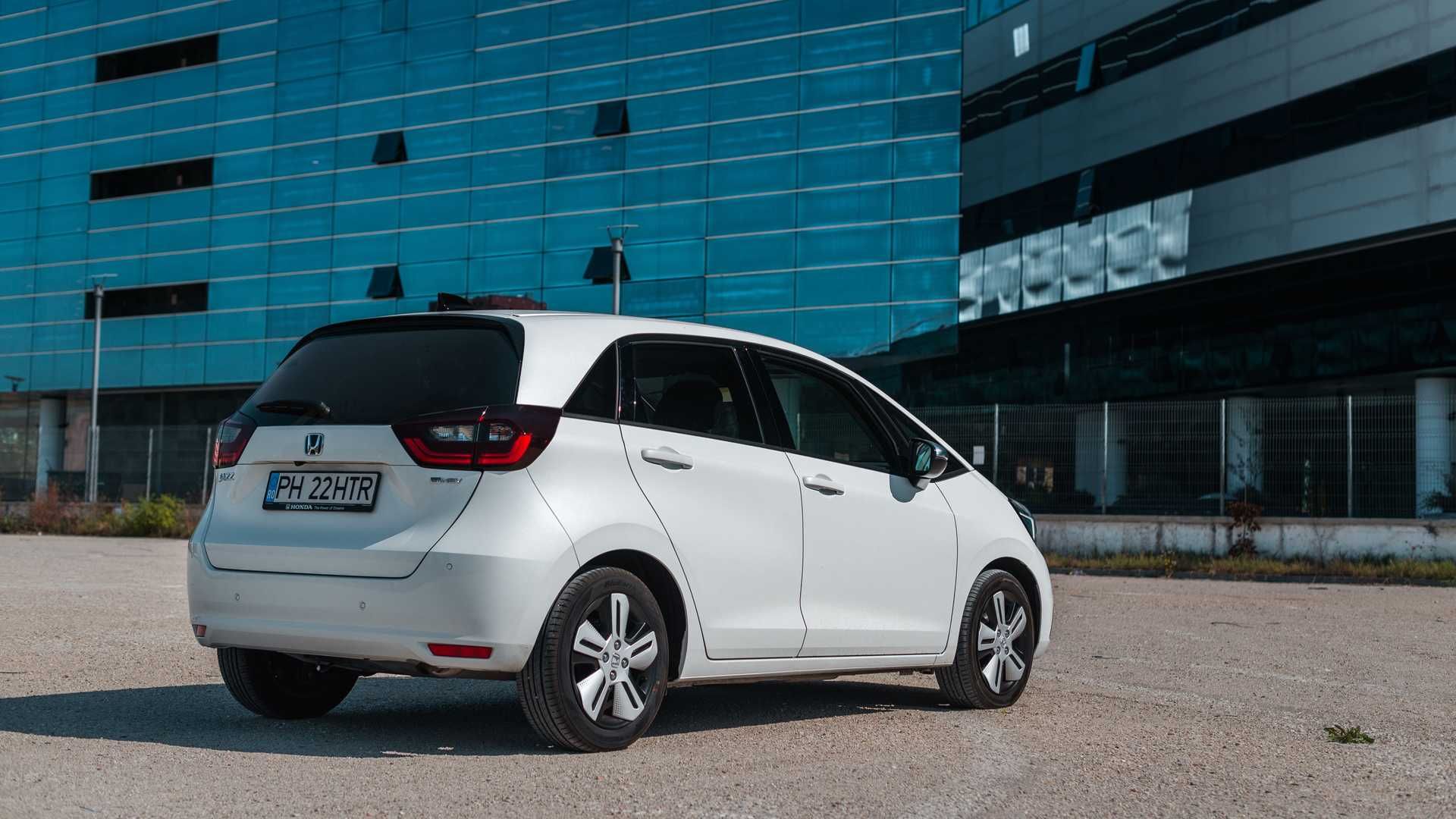 نمای سه چهارم عقب خودروی هیبریدی / Hybrid car هوندا جاز فیت / 2020 Honda Jazz (Fit) e:HEV سفید رنگ با منظره ساختمان