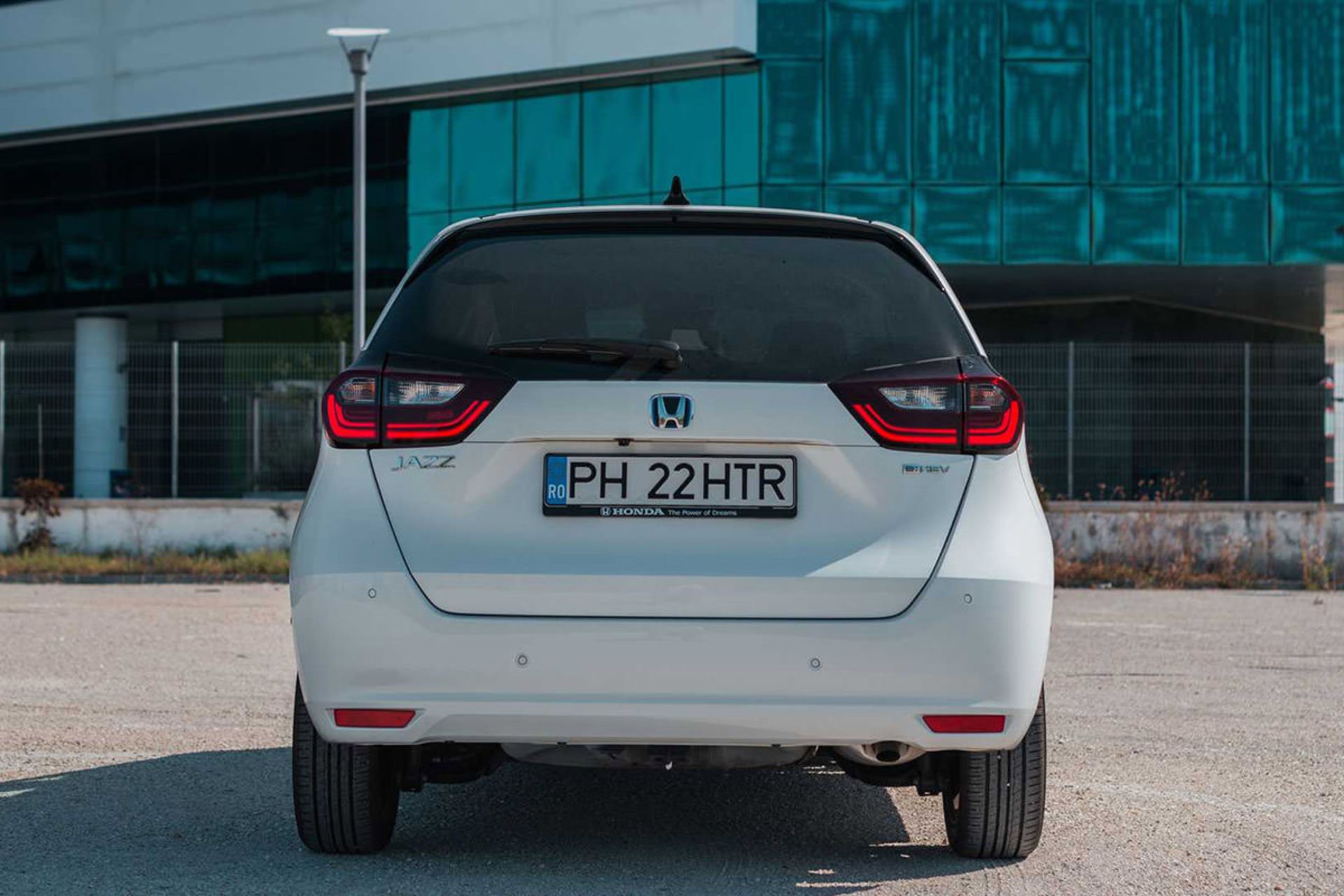 نمای عقب خودروی هیبریدی / Hybrid car هوندا جاز فیت / 2020 Honda Jazz (Fit) e:HEV سفید رنگ با منظره ساختمان