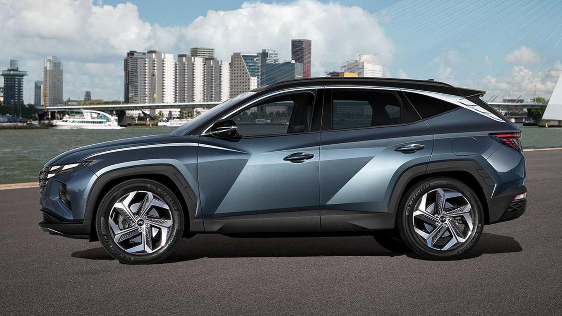 نمای جانبی خودرو کراس اور هیوندای توسان 2022 / 2022 Hyundai Tucson crossover با رنگ آبی در کنار ساختمان و آسمان آبی با ابر