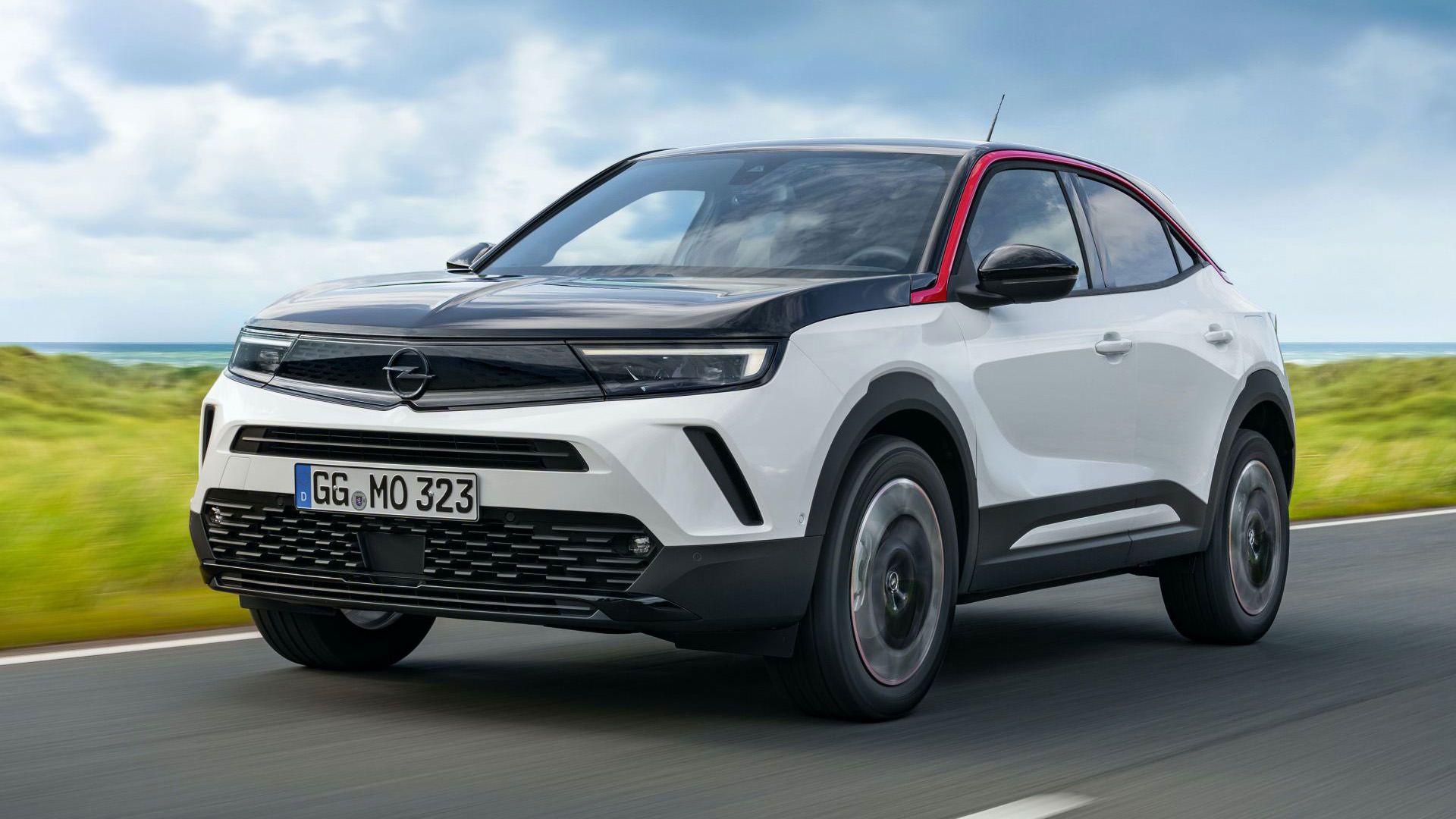 نمای سه چهارم کراس اور کامپکت اوپل موکا 2021 / Opel Mokka با طرح دو رنگ سفید و مشکی در جاده با منظره آسمان ابری