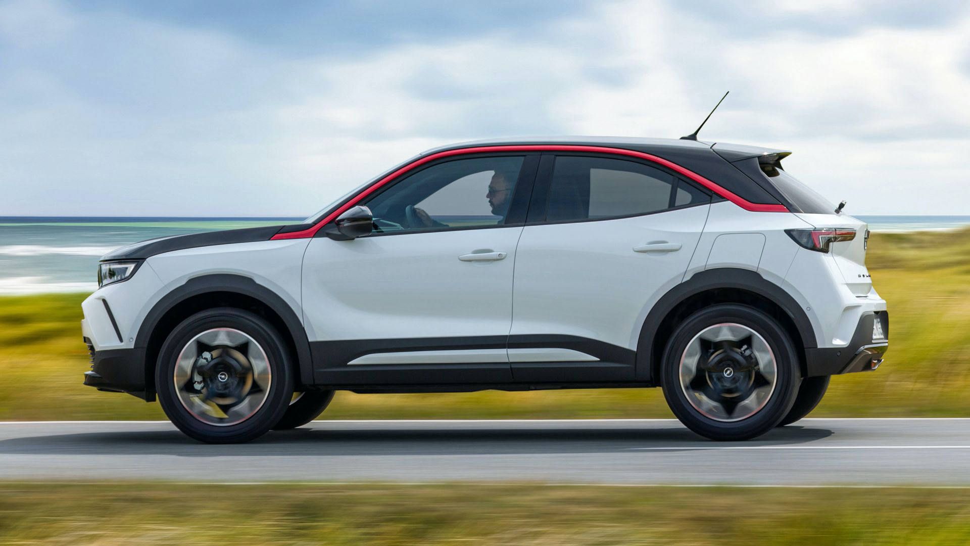 نمای جانبی کراس اور کامپکت اوپل موکا 2021 / Opel Mokka با طرح دو رنگ سفید و مشکی در جاده با منظره آسمان آبی