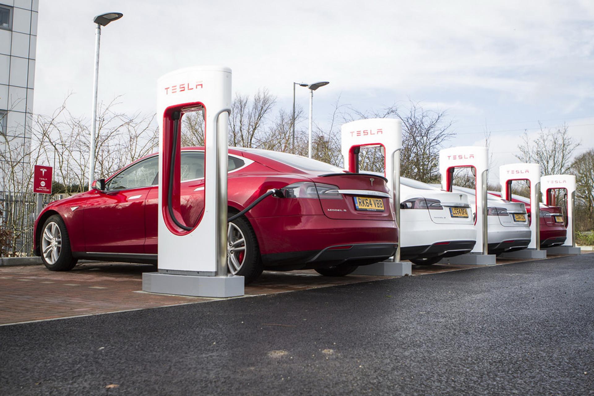 خودروی الکتریکی / electric car تسلا قرمز در حال شارژ توسط ایستگاه شارژ کنار خیابان