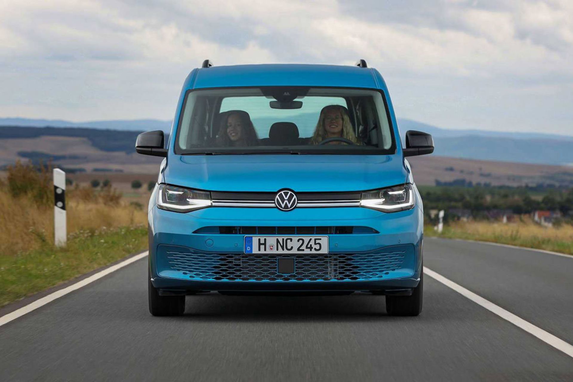 نمای جلو ون کمپر تفریحی فولکس واگن کدی کالیفرنیا / Volkswagen Caddy California Camper Van آبی رنگ در جاده با نمای آسمان ابری