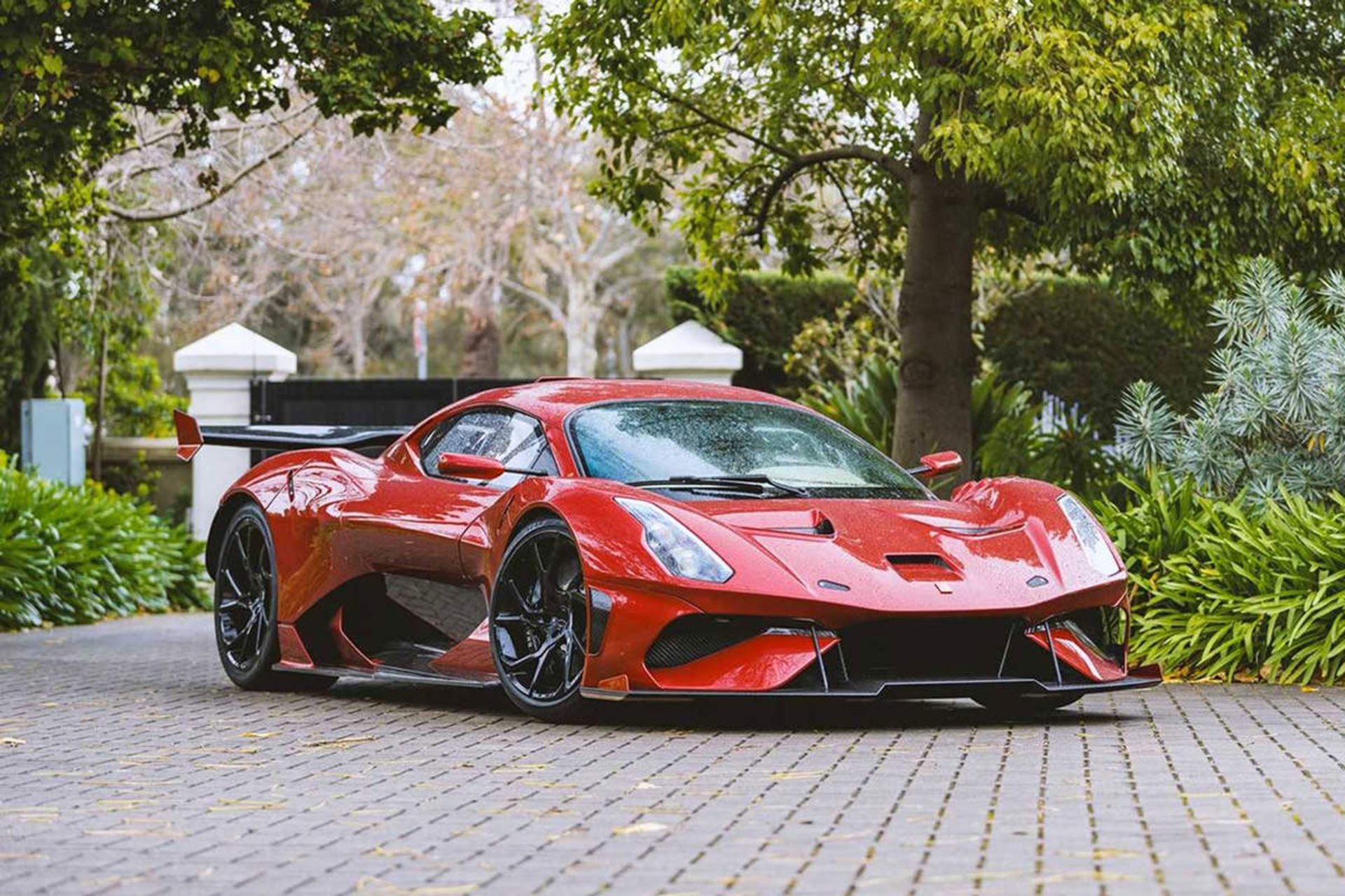 نمای جلو خودرو سوپراسپرت برابهام / Brabham BT62R قرمز رنگ با منظره درخت در سنگ فرش