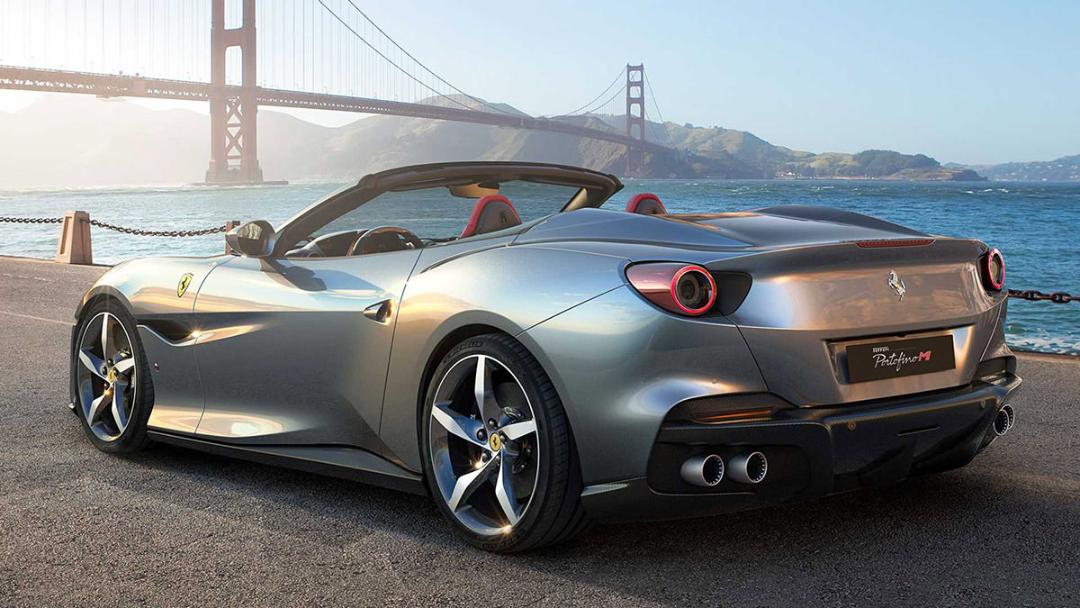 نمای عقب خودرو روباز فراری پورتوفینو ام / Ferrari Portofino M نقره ای رنگ در کنار دریا و پل معلق