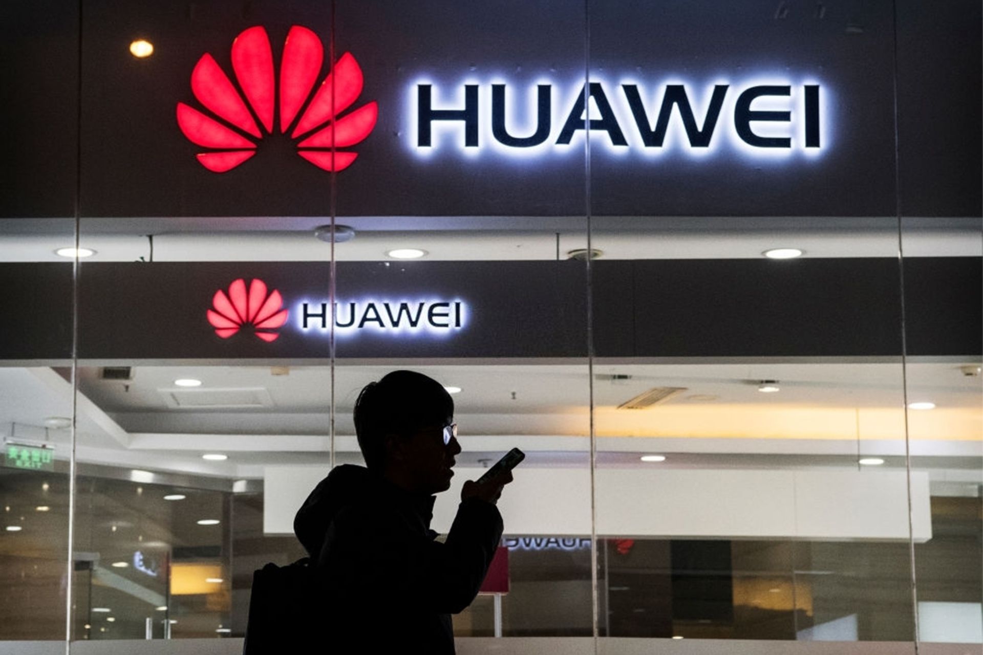 لوگو هواوی / Huawei روی ساختمان، فردی درحال صحبت با تلفن