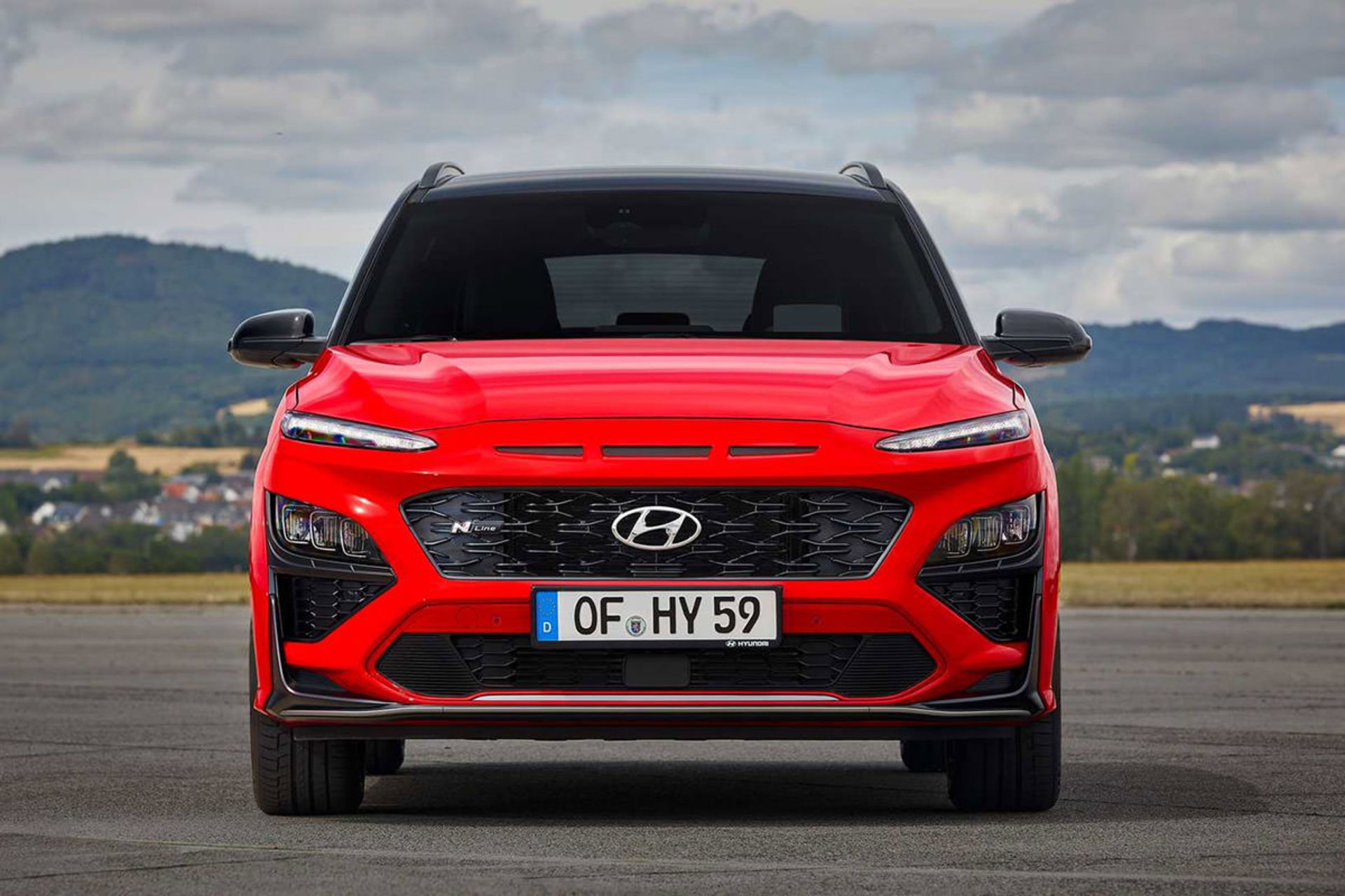 نمای جلو کراس اور هیوندای کنا ان لاین / Hyundai Kona N-Line crossover قرمز رنگ با زمینه آسمان ابری