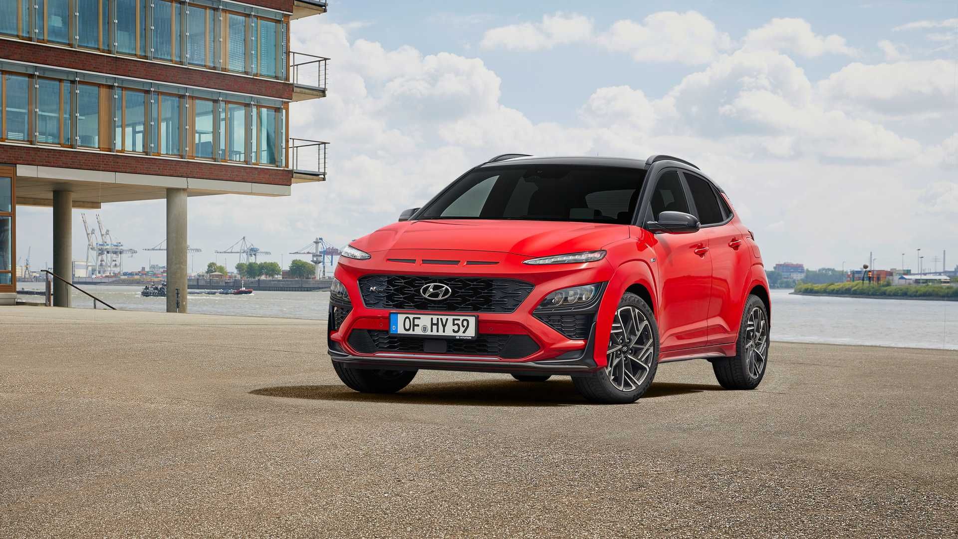 نمای جلو کراس اور هیوندای کنا ان لاین / Hyundai Kona N-Line crossover قرمز رنگ با زمینه آسمان آبی در کنار ساختمان