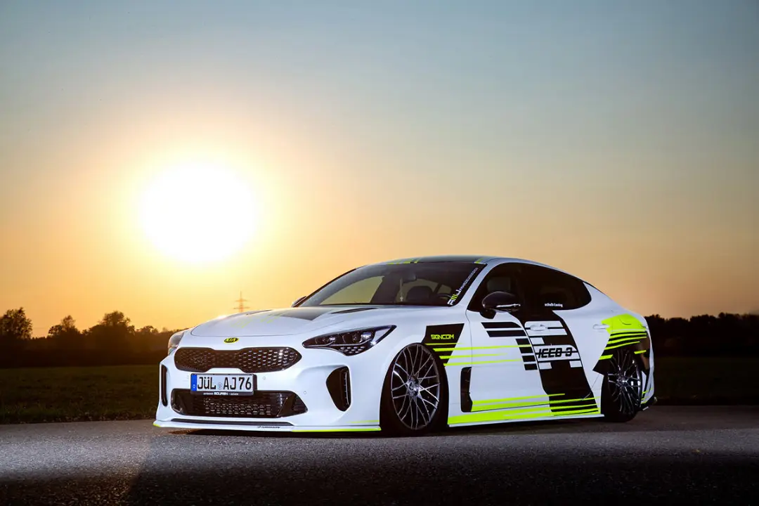 نمای سه چهارم جلو کیا استینگر / Kia Stinger سفید رنگ با تزئینات نئون و منظره غروب خورشید