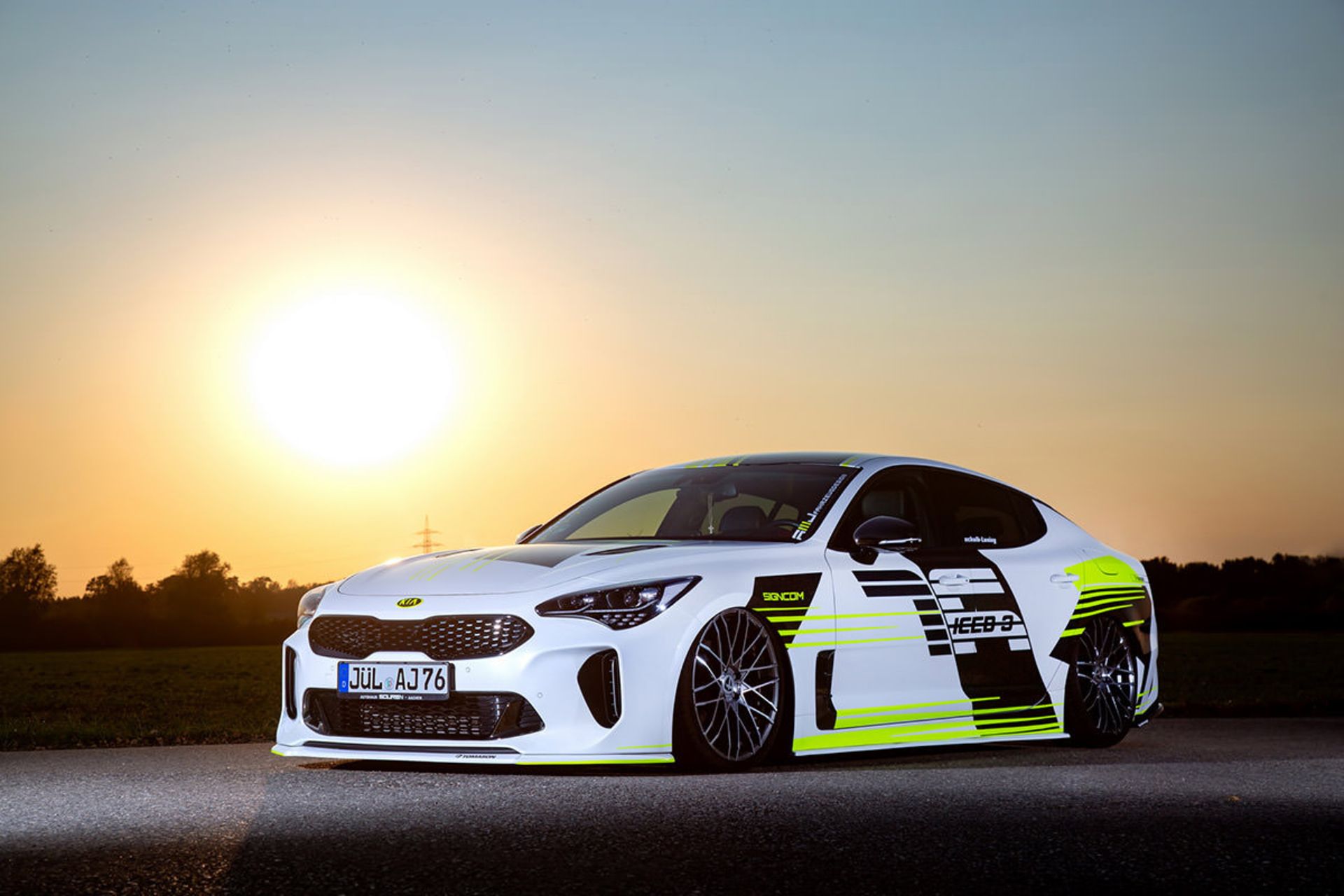 نمای سه چهارم جلو کیا استینگر / Kia Stinger سفید رنگ با تزئینات نئون و منظره غروب خورشید