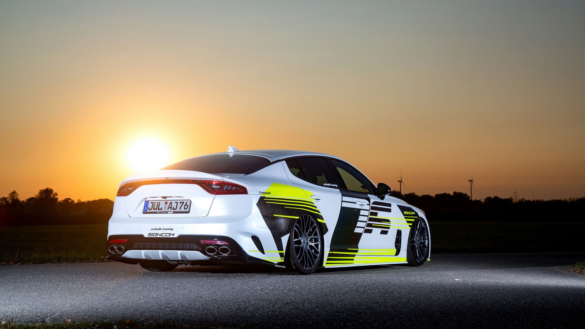 نمای سه چهارم عقب کیا استینگر / Kia Stinger سفید رنگ با تزئینات نئون و منظره غروب خورشید