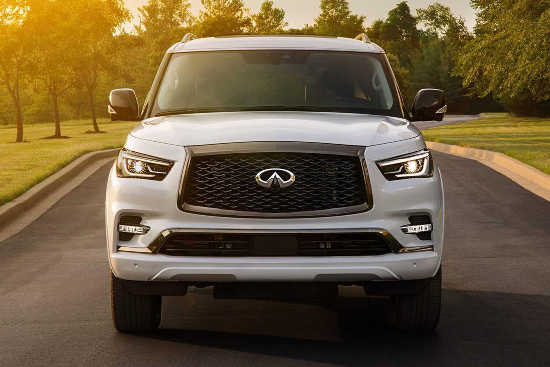 نمای جلو خودرو شاسی بلند لوکس اینفینیتی کیو ایکس 80 / 2021 Infiniti QX80 SUV سفید رنگ در جاده با زمینه درخت
