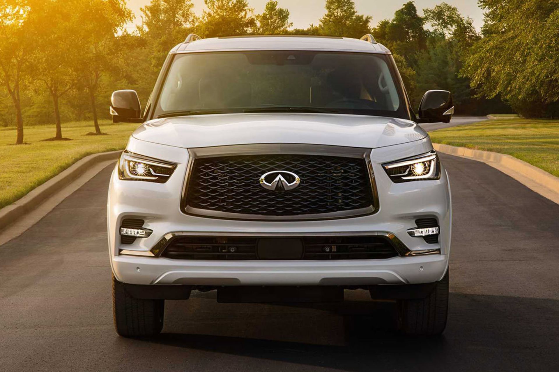 نمای جلو خودرو شاسی بلند لوکس اینفینیتی کیو ایکس 80 / 2021 Infiniti QX80 SUV سفید رنگ در جاده با زمینه درخت