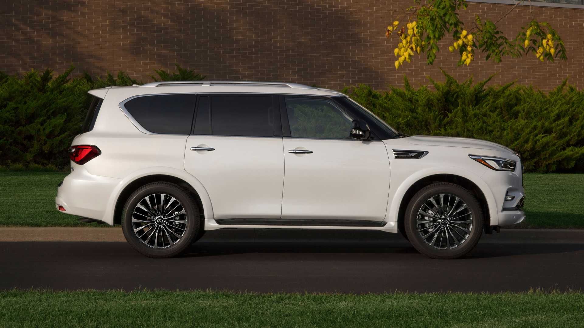 نمای جانبی خودرو شاسی بلند لوکس اینفینیتی کیو ایکس 80 / 2021 Infiniti QX80 SUV سفید رنگ در جاده با زمینه درخت