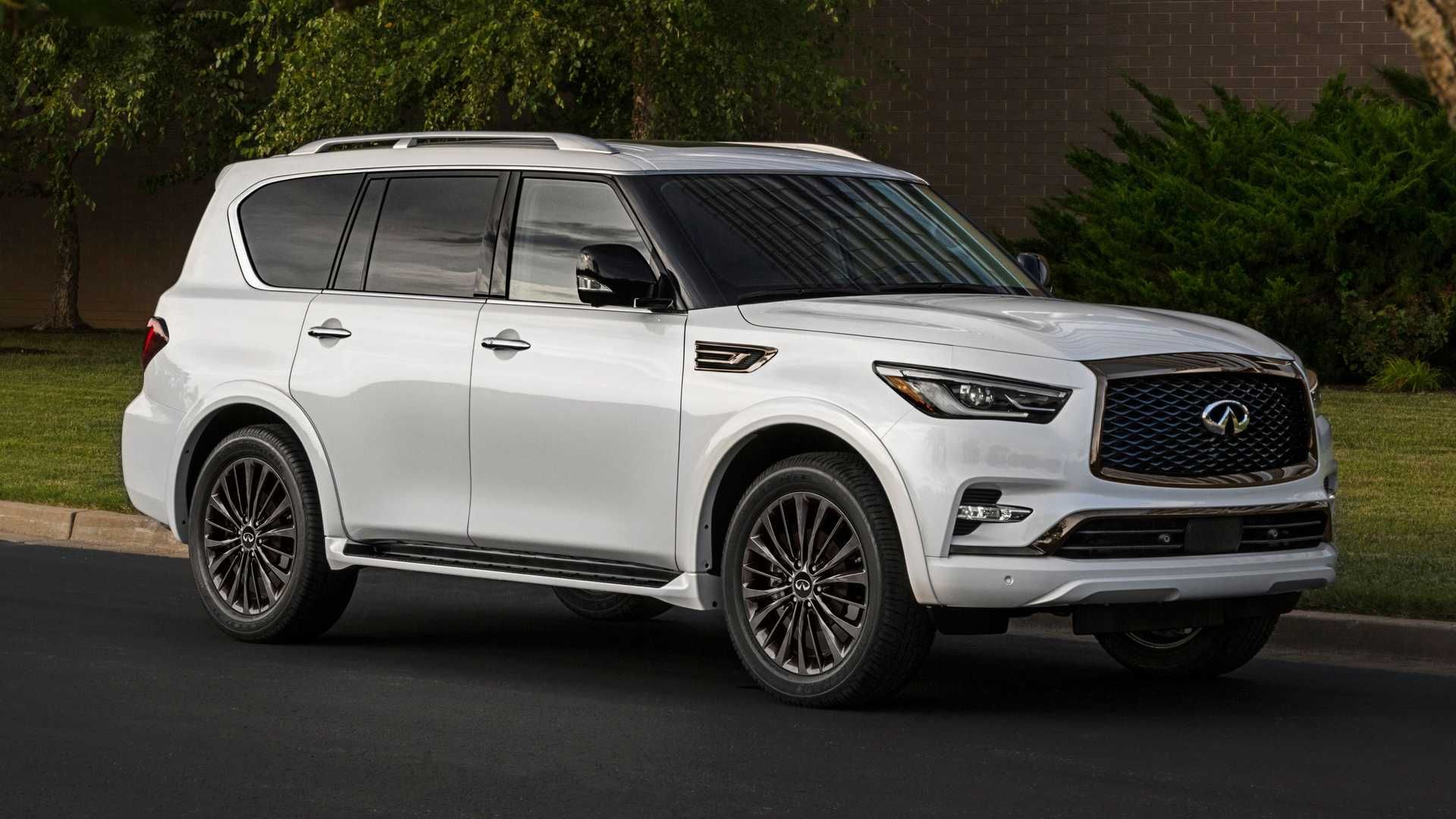 نمای جلو چپ خودرو شاسی بلند لوکس اینفینیتی کیو ایکس 80 / 2021 Infiniti QX80 SUV سفید رنگ در جاده با زمینه درخت