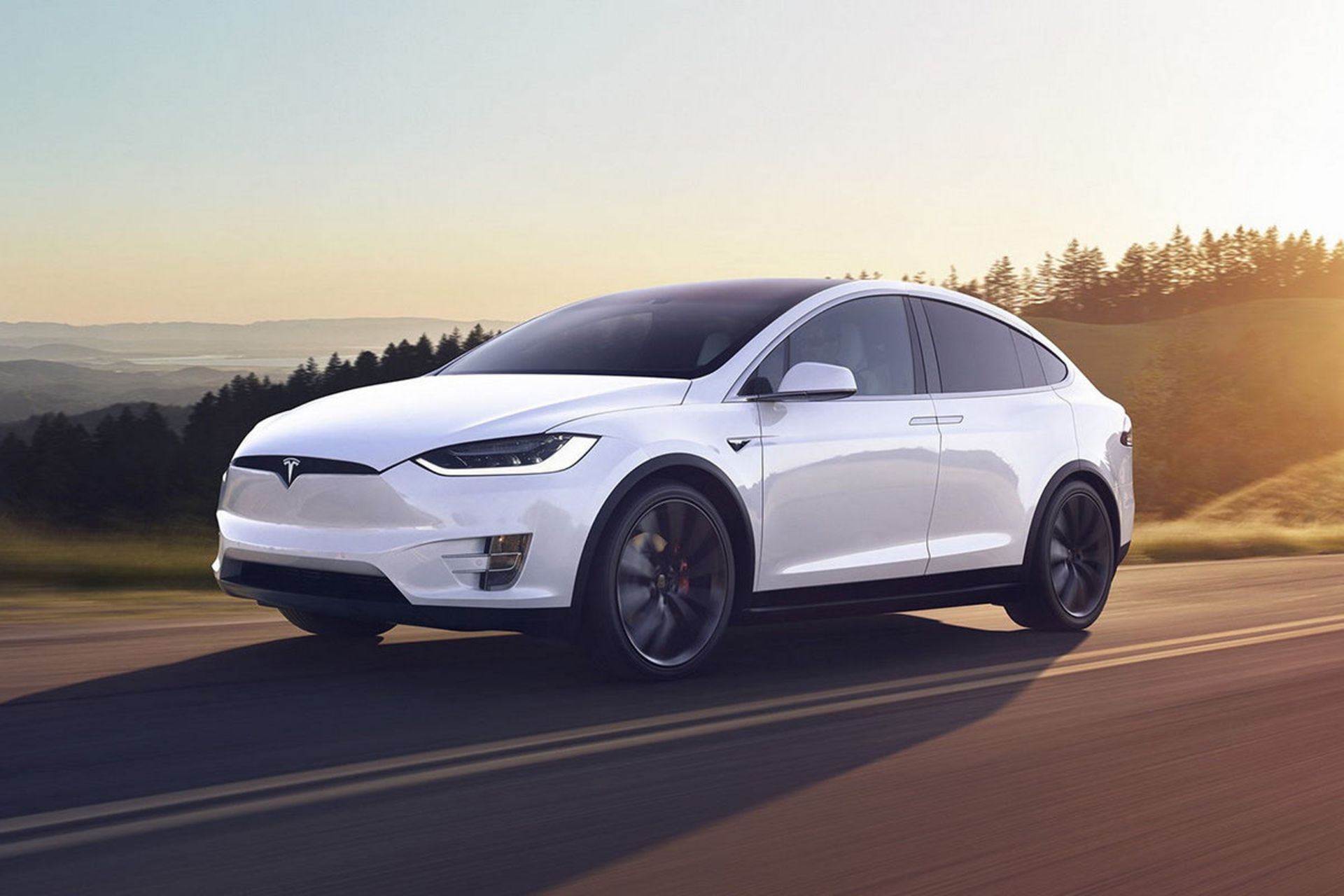 خودروی الکتریکی تسلا مدل ایکس / tesla model x سفید رنگ در جاده با منظره درخت و آسمان