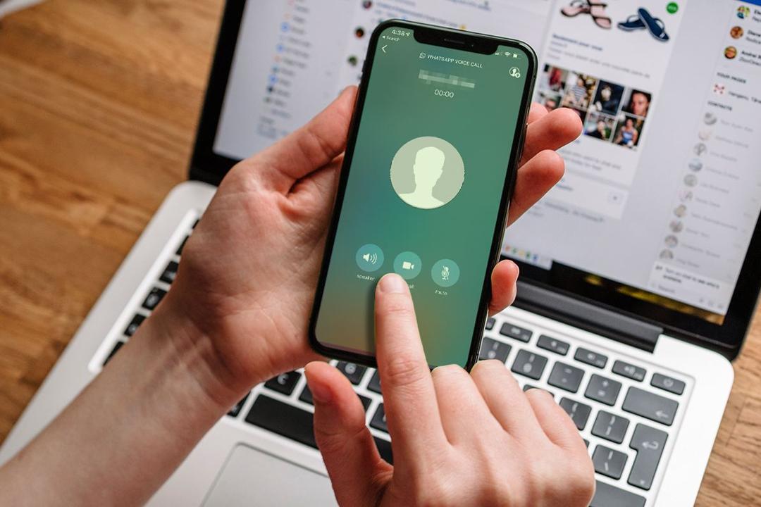 آیفون با واتساپ / WhatsApp در دست کاربر بالای لپ تاپ