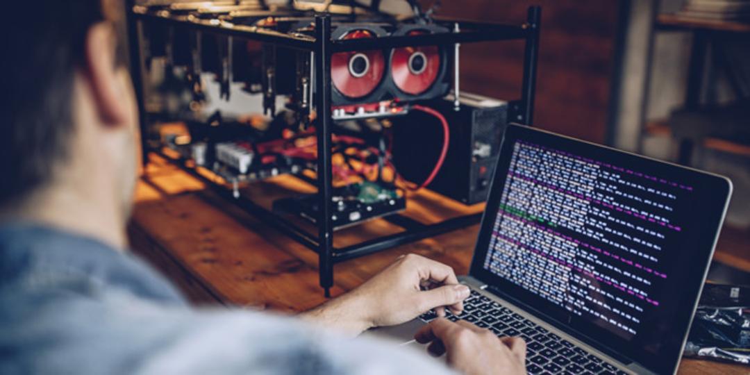 کاربر درحال استخراج بیت کوین / Bitcoin و نگاه به لپ‌تاپ روی میز چوبی