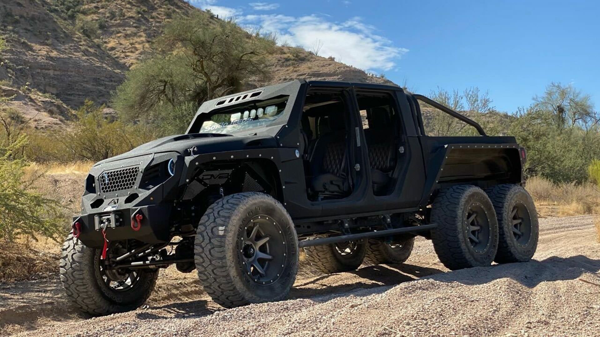 نمای سه چهارم جیپ گلادیاتور / Jeep Gladiator مجهز به 6 چرخ با منظره آسمان آبی و درخت