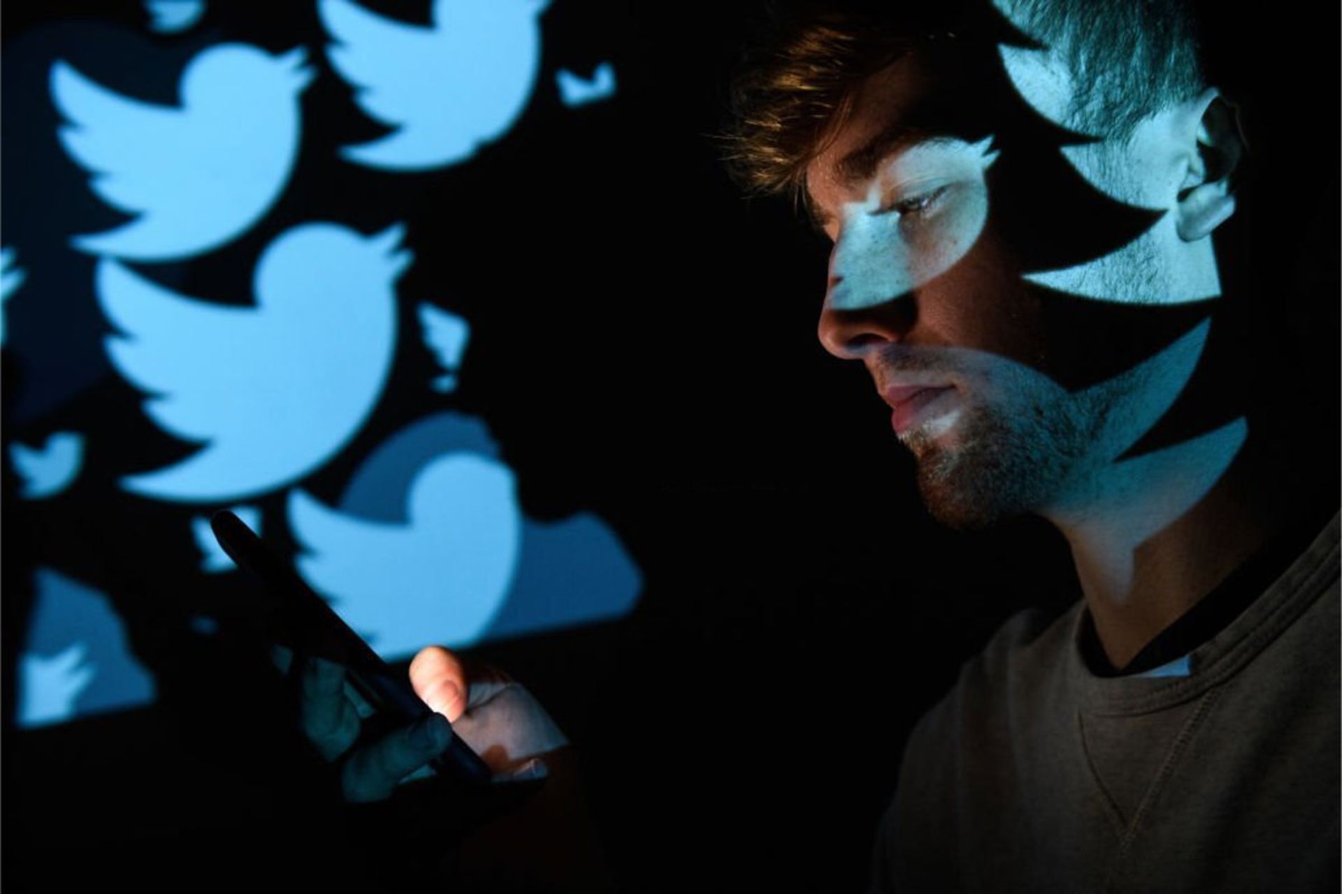 مرد جوان در حال استفاده از شبکه اجتماعی توییتر / Twitter روی گوشی