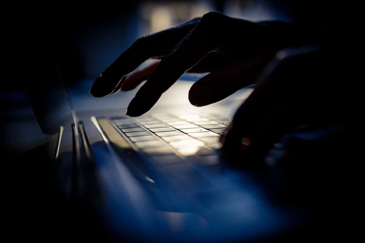 Hand typing on dark shadow laptop keyboard