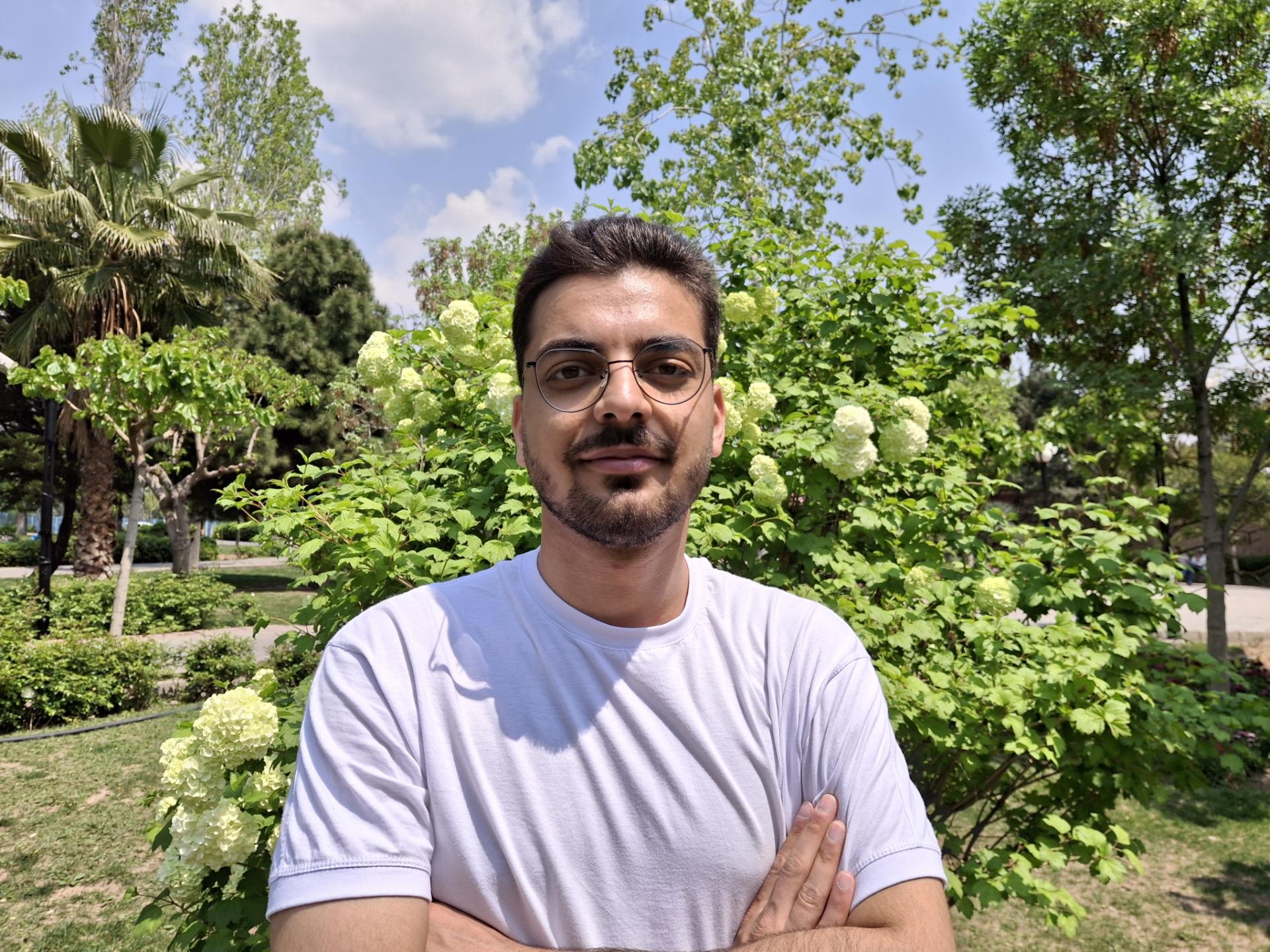 تصویر مرد جوان با تیشرت سفید در نور روز در یک پارک با دوربین گلکسی A35