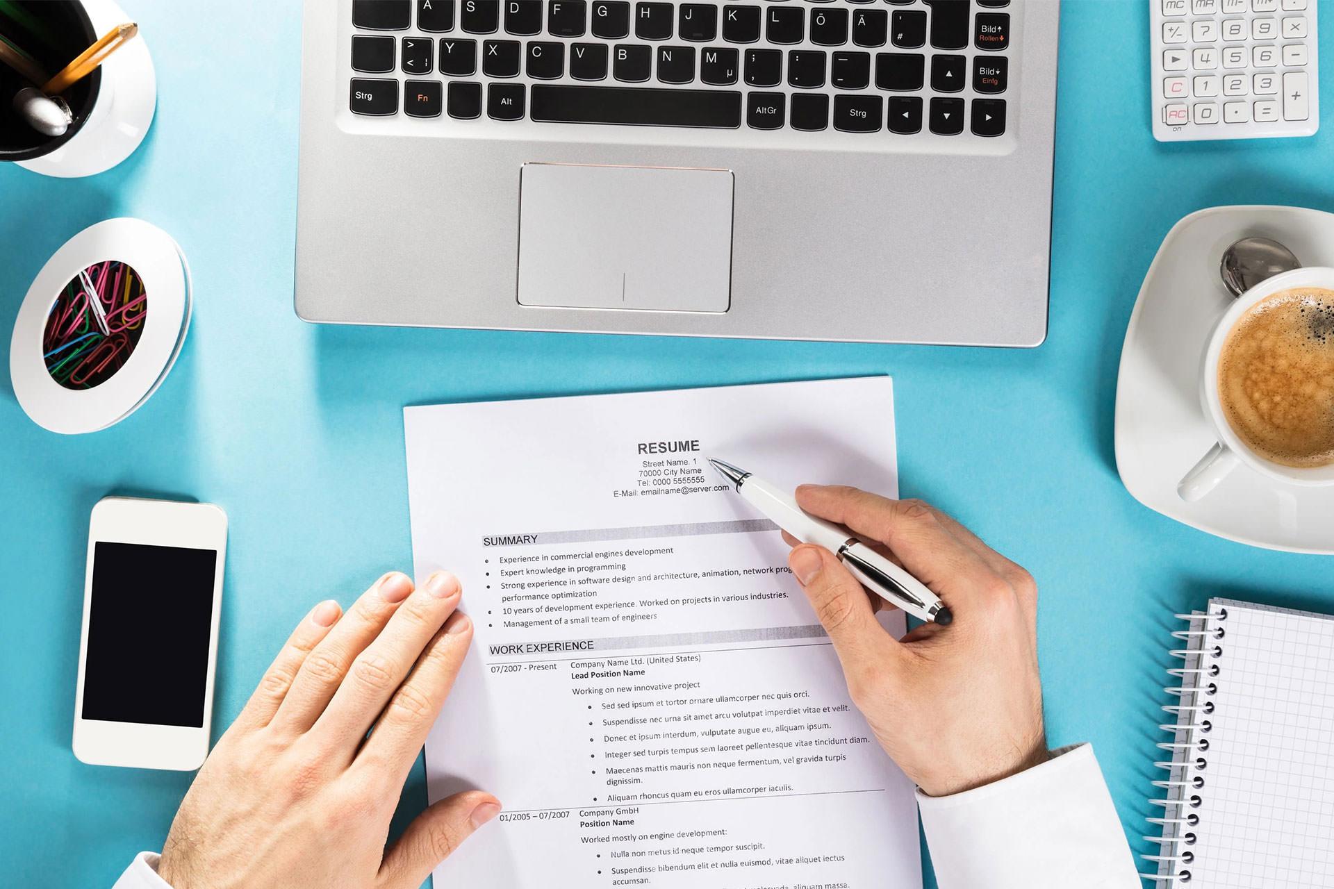  دستان مرد روی کاغذ روی میز جلوی لپ‌تاپ و فنجان قهوه