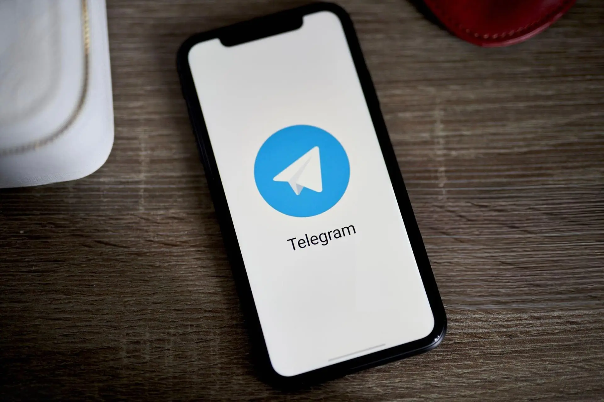 لوگو تلگرام / Telegram در نمایشگر آیفون ۱۲ روی میز
