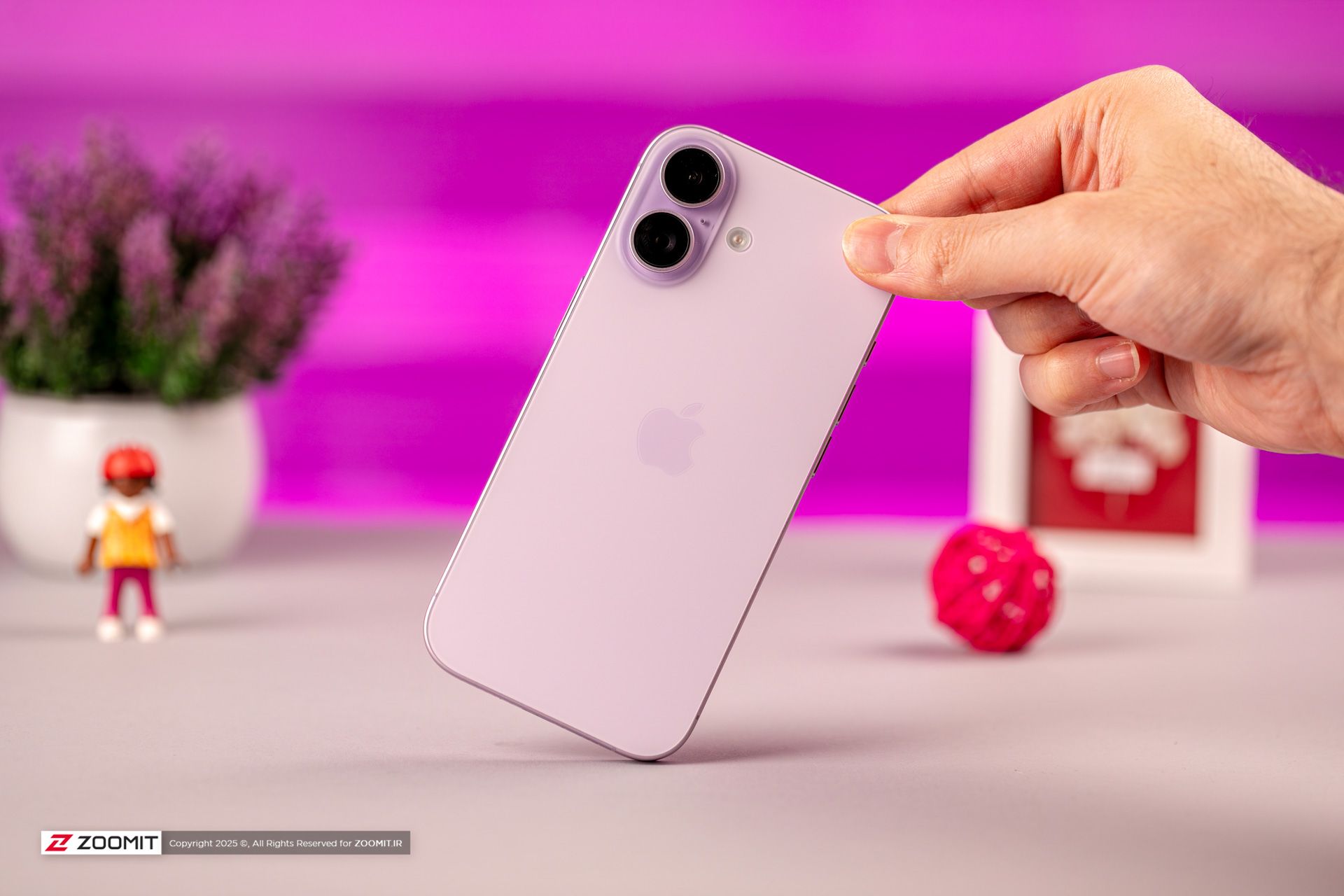 آیفون بنفش ایستاده روی میز با پس‌زمینه بنفش و اشیای دکوری