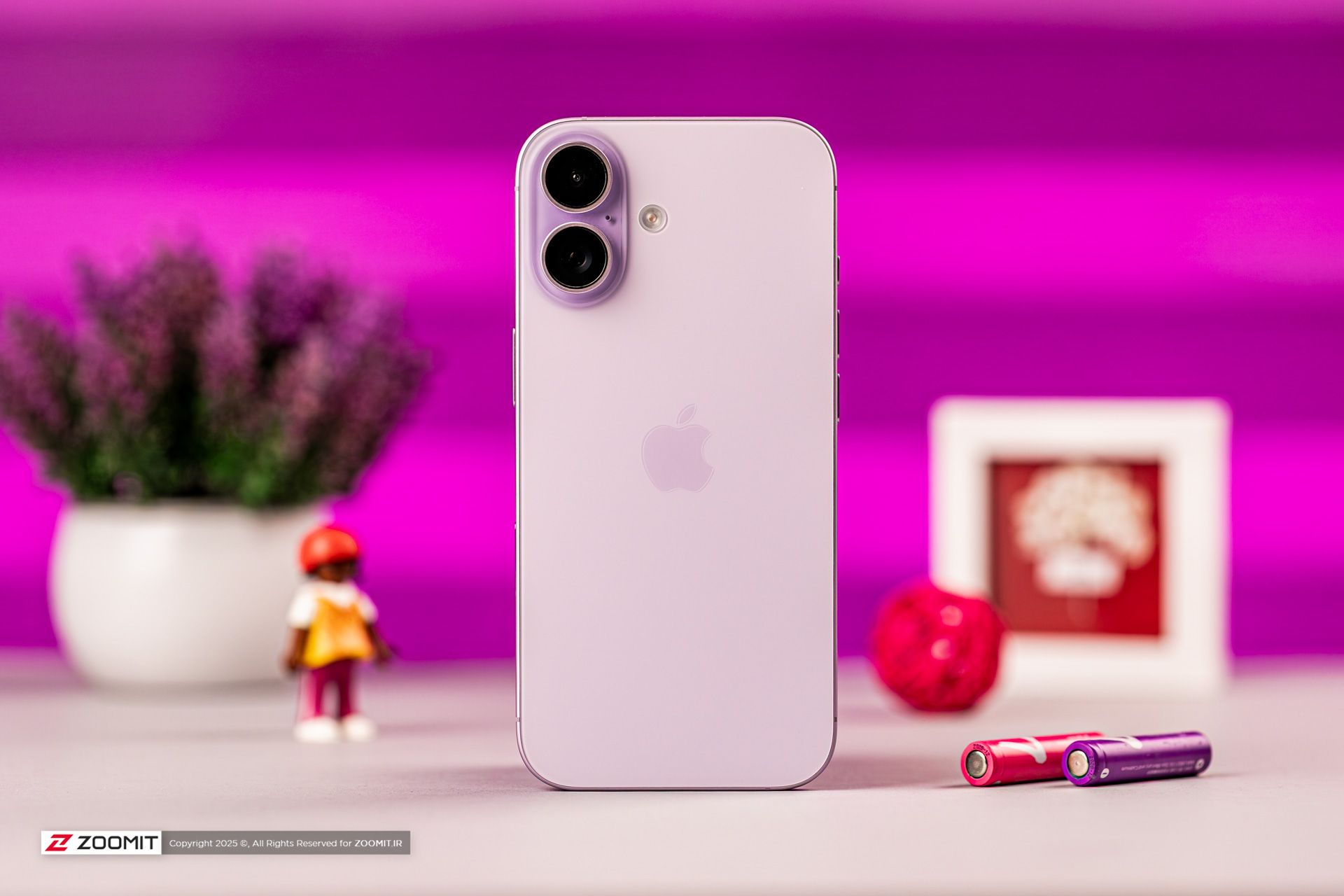 پشت آیفون بنفش روی میز با پس‌زمینه بنفش و باتری‌های رنگی