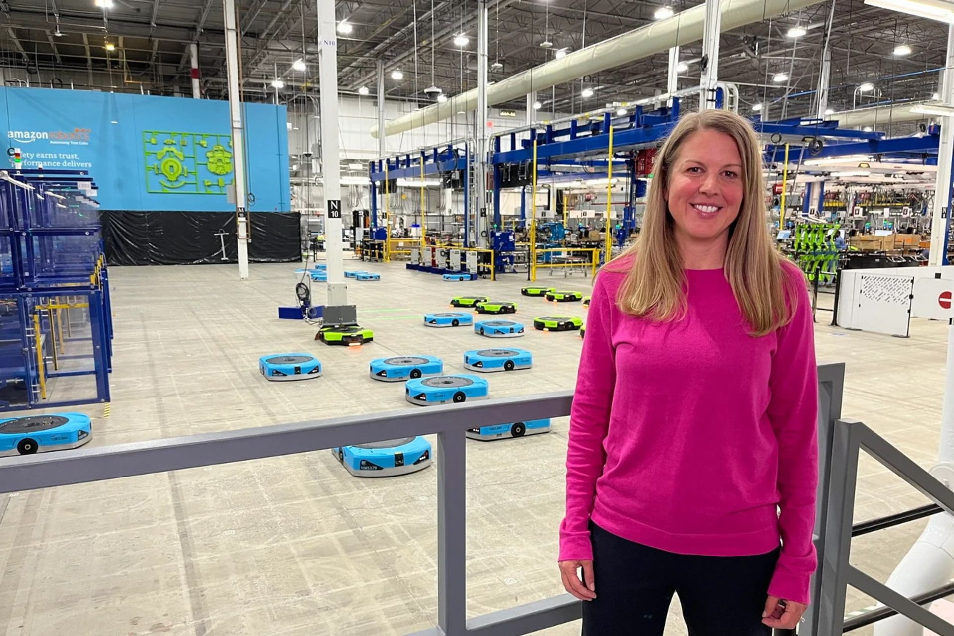اریکا مک‌کلاسکی، مدیر بخش تولید و عملیات فنی در Amazon Robotics- زنی با لبخند در لباس صورتی در کارگاهی بزرگ