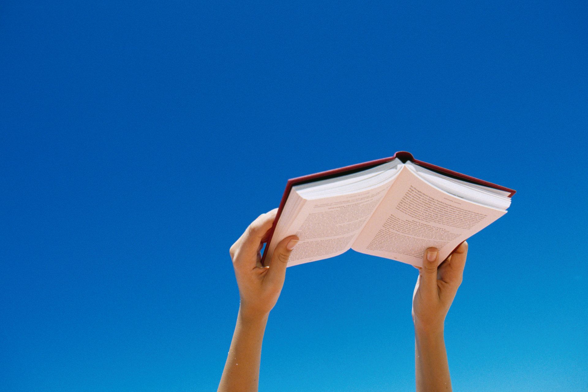 کتاب در دست به سمت آسمان با پس زمین آبی آسمان