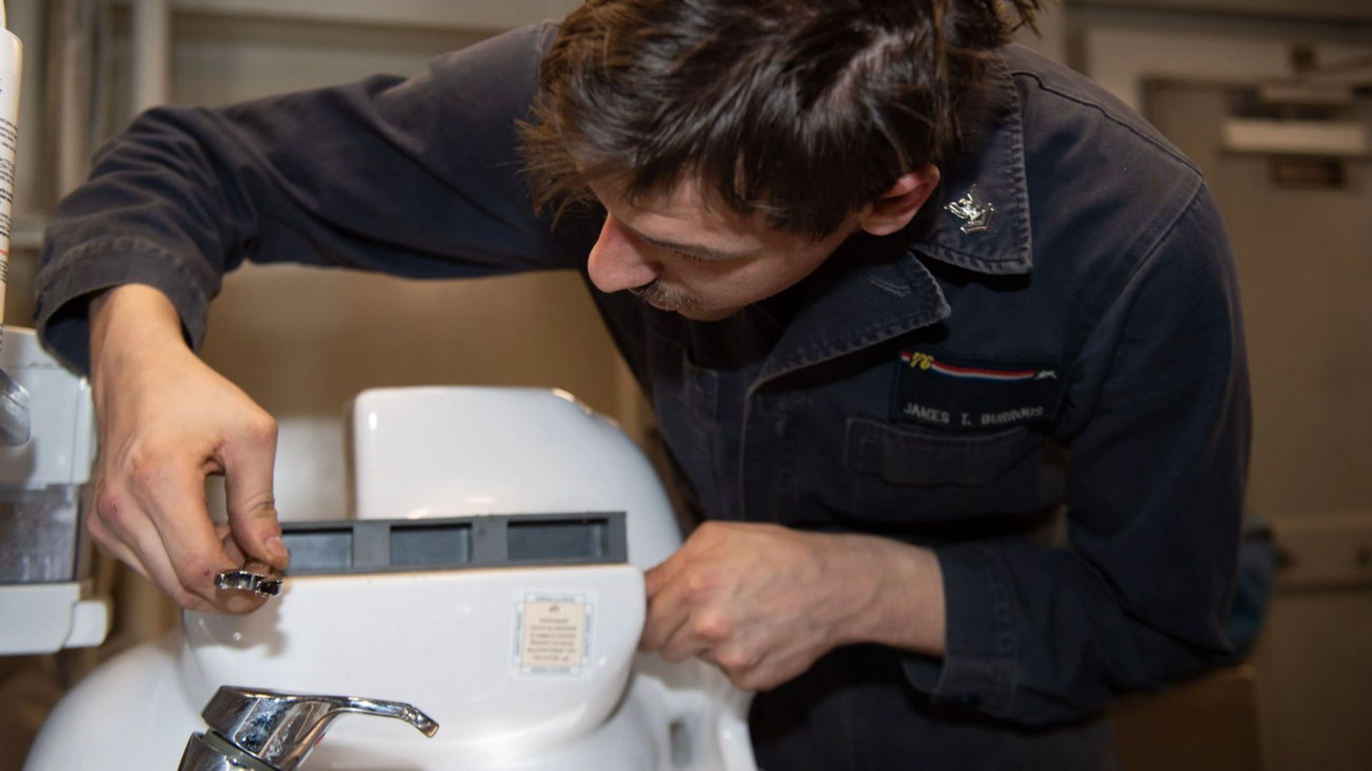 یک تکنسین نیروی دریایی در حال کار بر روی توالت یک ناو هواپیمابر