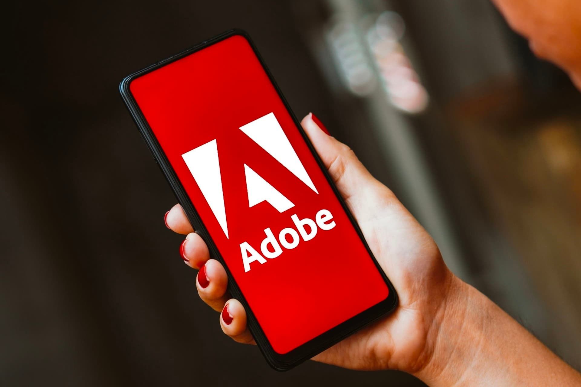 لوگو ادوبی / Adobe در داخل موبایل در دست راست یک زن
