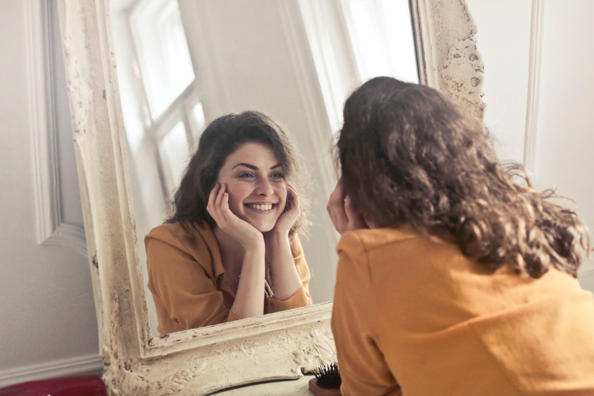 زن جوان با لباس نارنجی به آینه لبخند می‌زند
