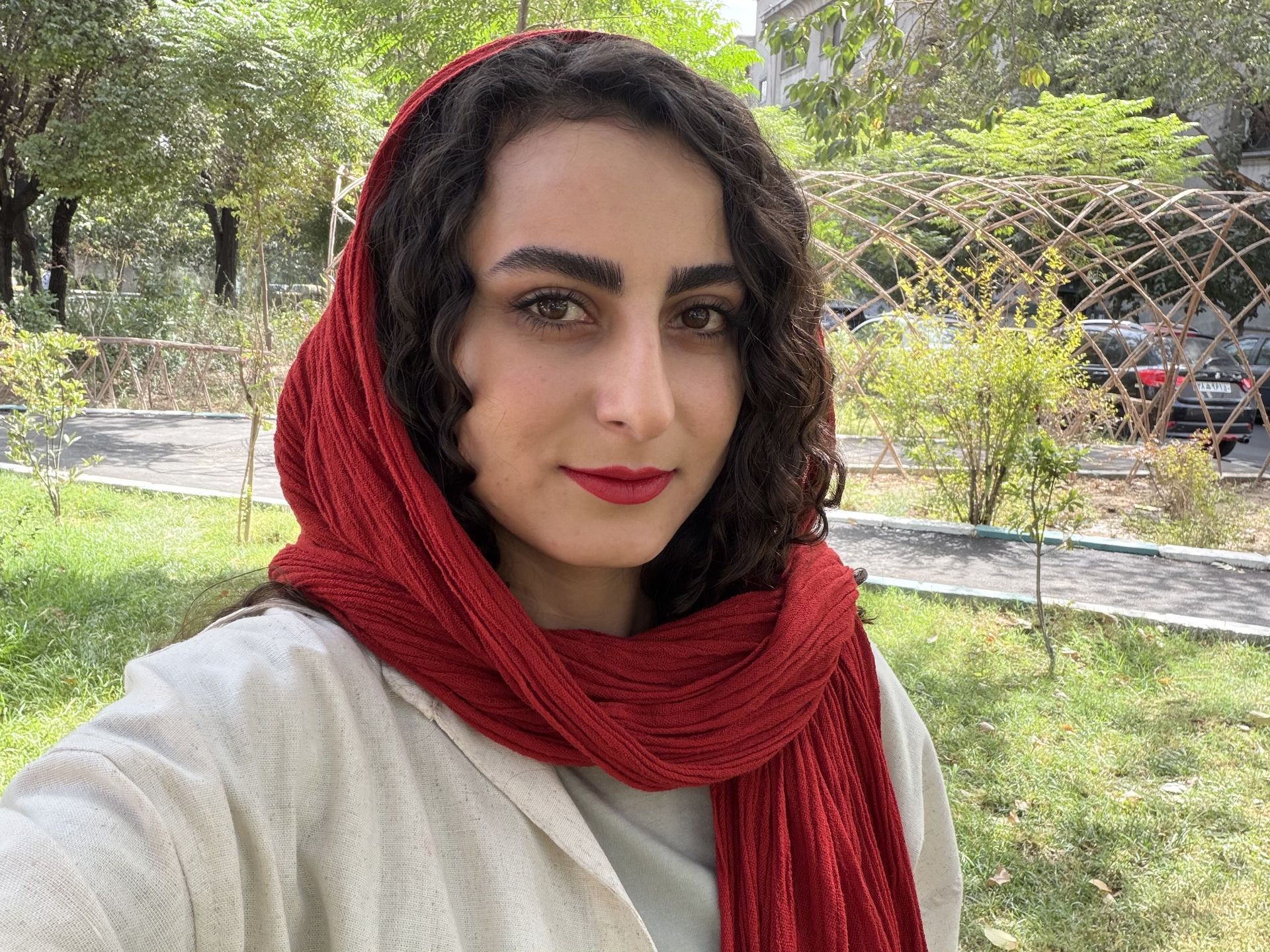 سلفی زن با روسری قرمز و لباس روشن در یک پارک در روز آفتابی
